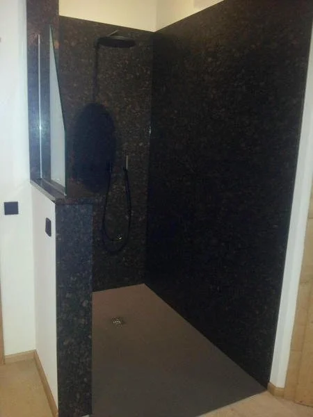 Eine Dusche mit dunklem Stein, eine Duschbrause und eine Handbrause, umgeben von weißen Wänden.