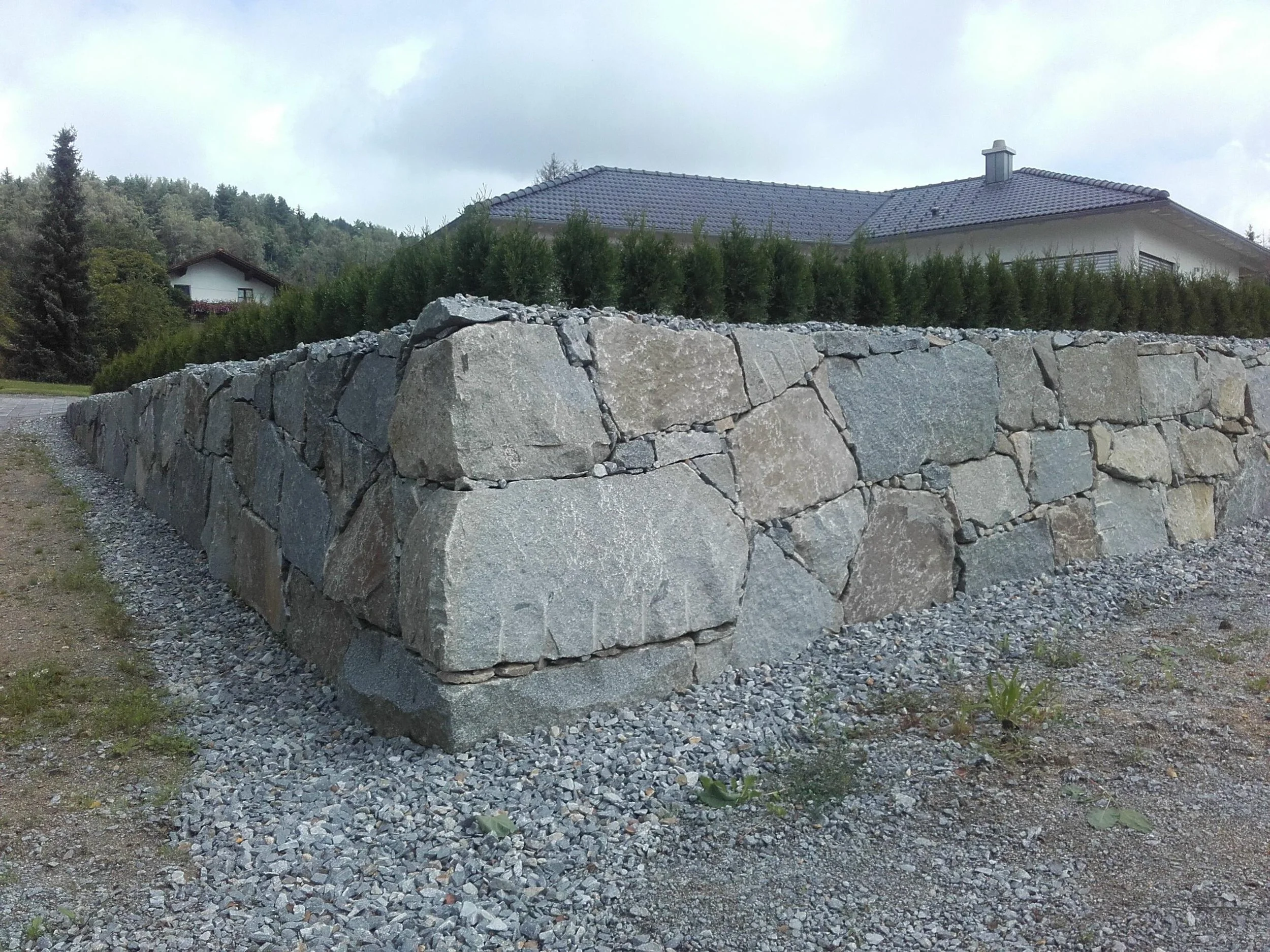 Ein gemauerter Findenschutthügel vor einem Haus mit Dach.