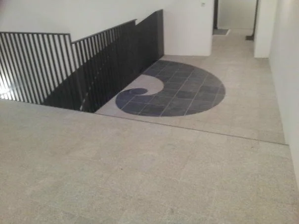 Ein Treppenabsatz mit einem Spiralmuster im Boden, das durch Fliesen in Schwarz und Grau gestaltet ist.