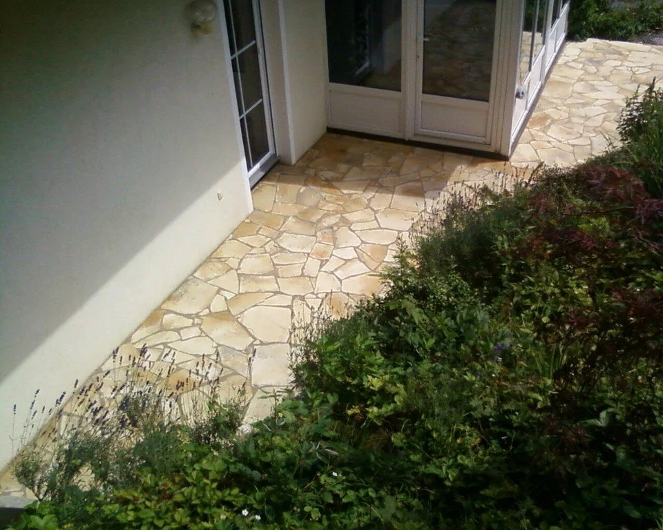 Ein gepflasterter Eingangsbereich mit einer Tür und umgeben von Gartenpflanzen.