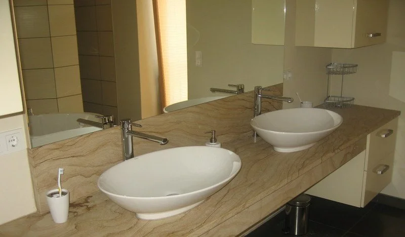 Zwei weiße Waschbecken auf einer luxuriösen Marmor-Waschplatte in einem modernen Badezimmer.