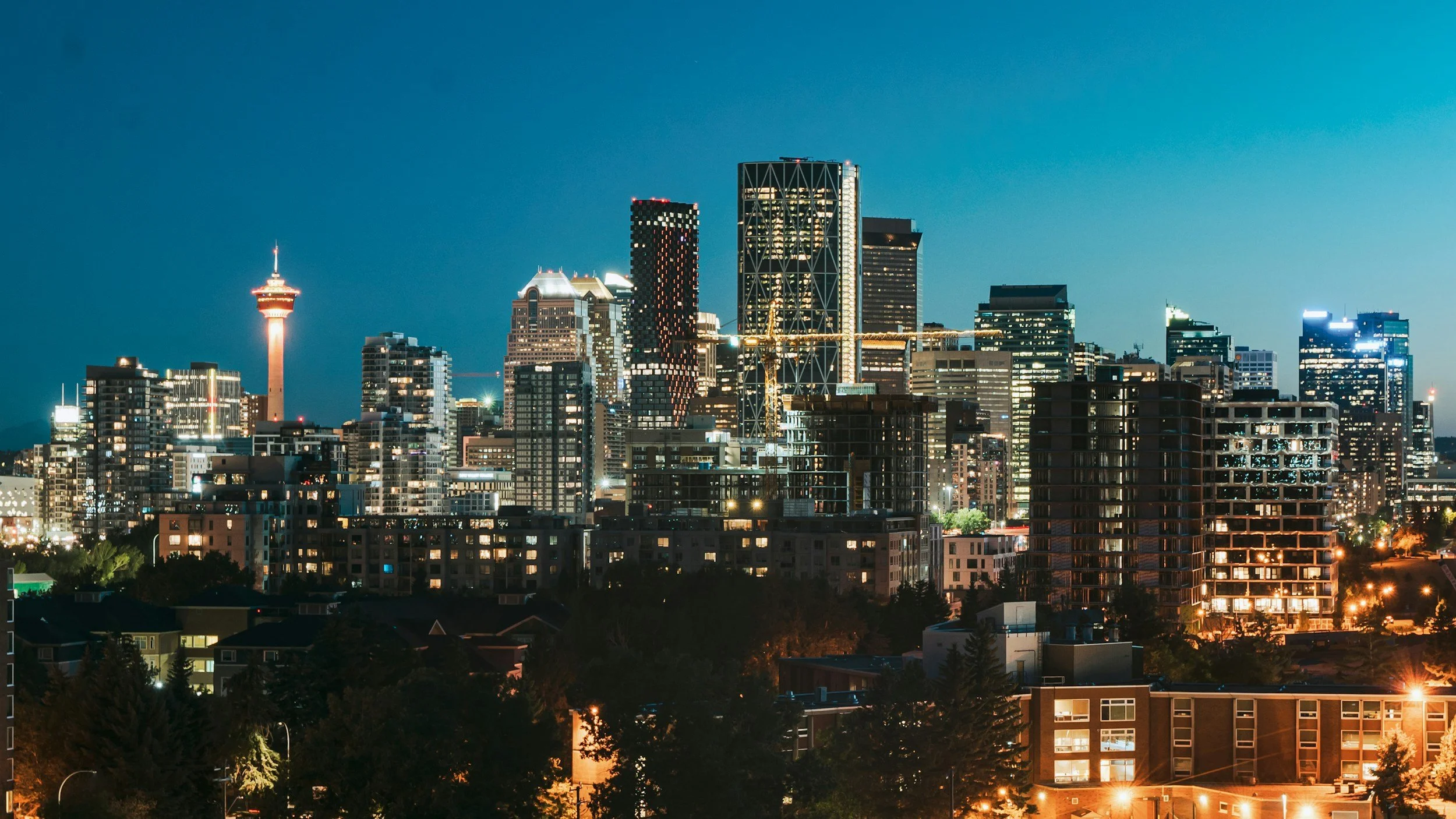 Nighttime city skyline with illuminated buildings and a tall tower, with a clear dark sky.