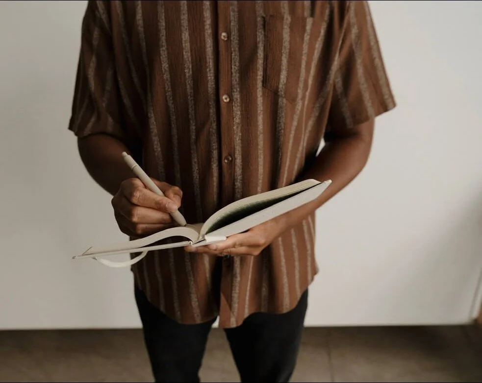 Male therapist wearing a brown shirt writing in a notebook
