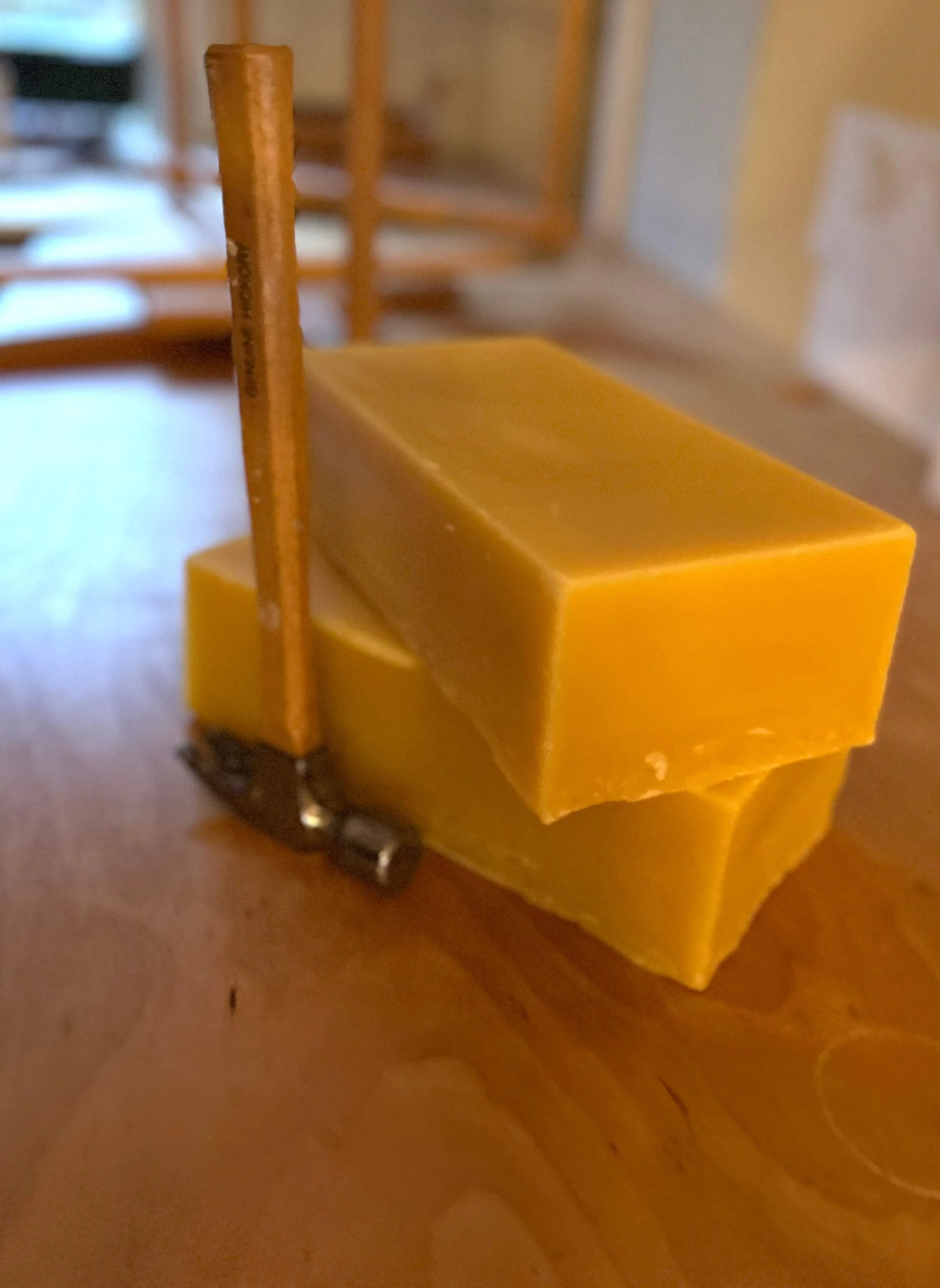 Two blocks of yellow beeswax with a small hammer.