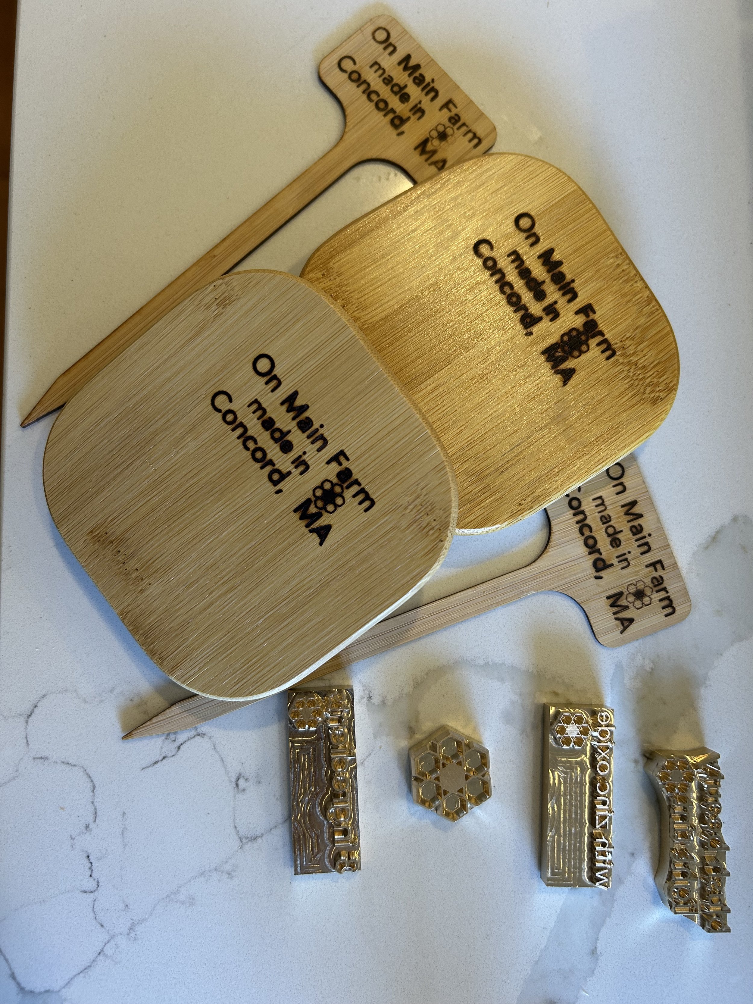 Collection of wooden and metallic custom stamps and stamps with the inscription "On Main Farm made in Concord, MA," placed on a white marble surface.