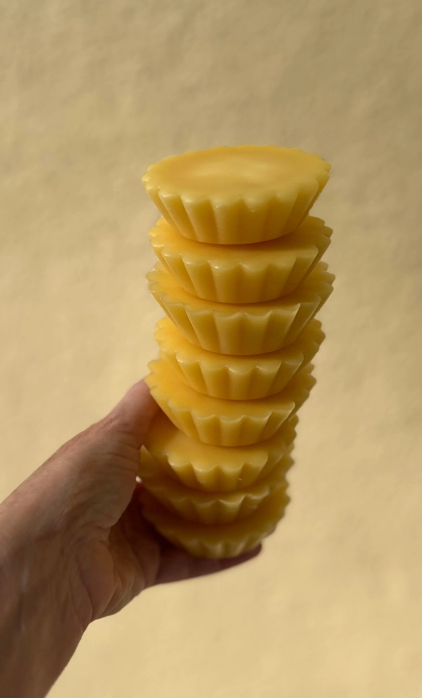 A hand holding a stack of yellow, fluted beeswax against a plain beige background.
