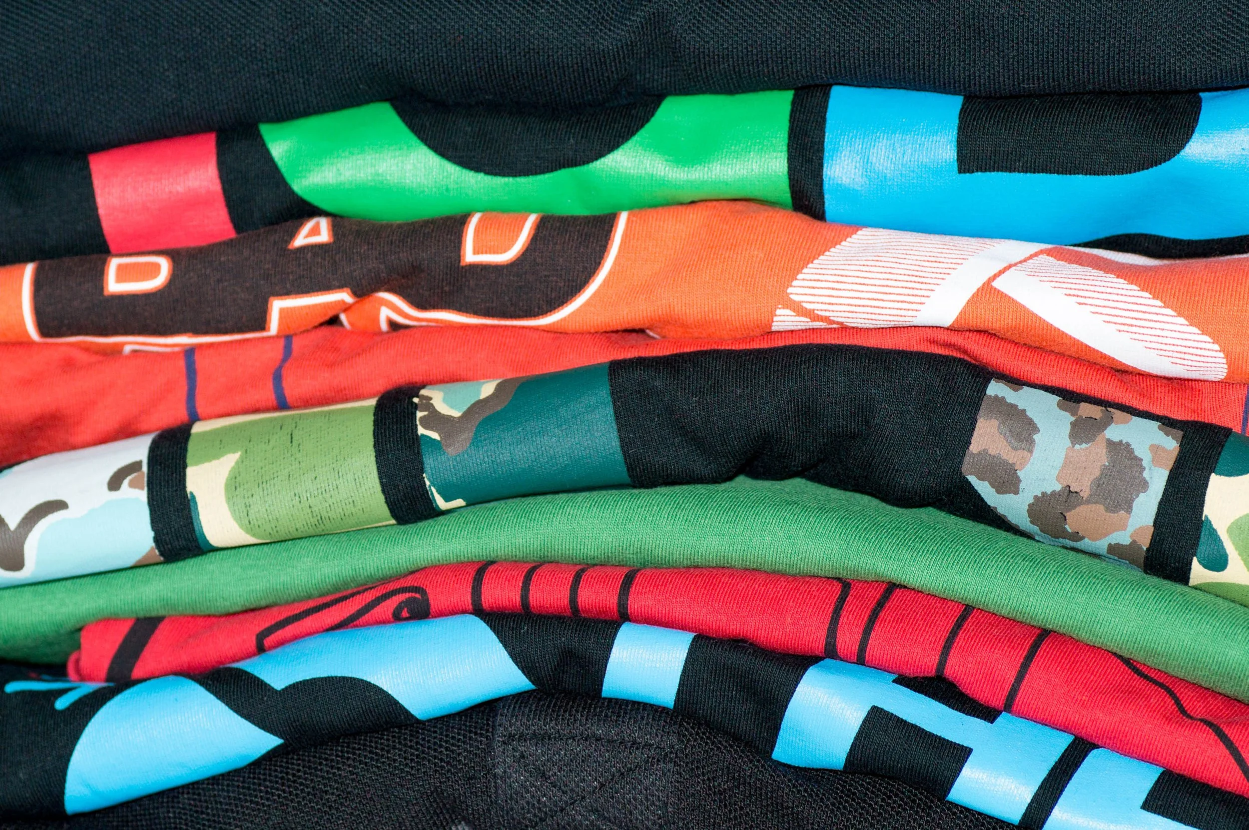 Stack of colorful folded t-shirts with various graphic designs and patterns.