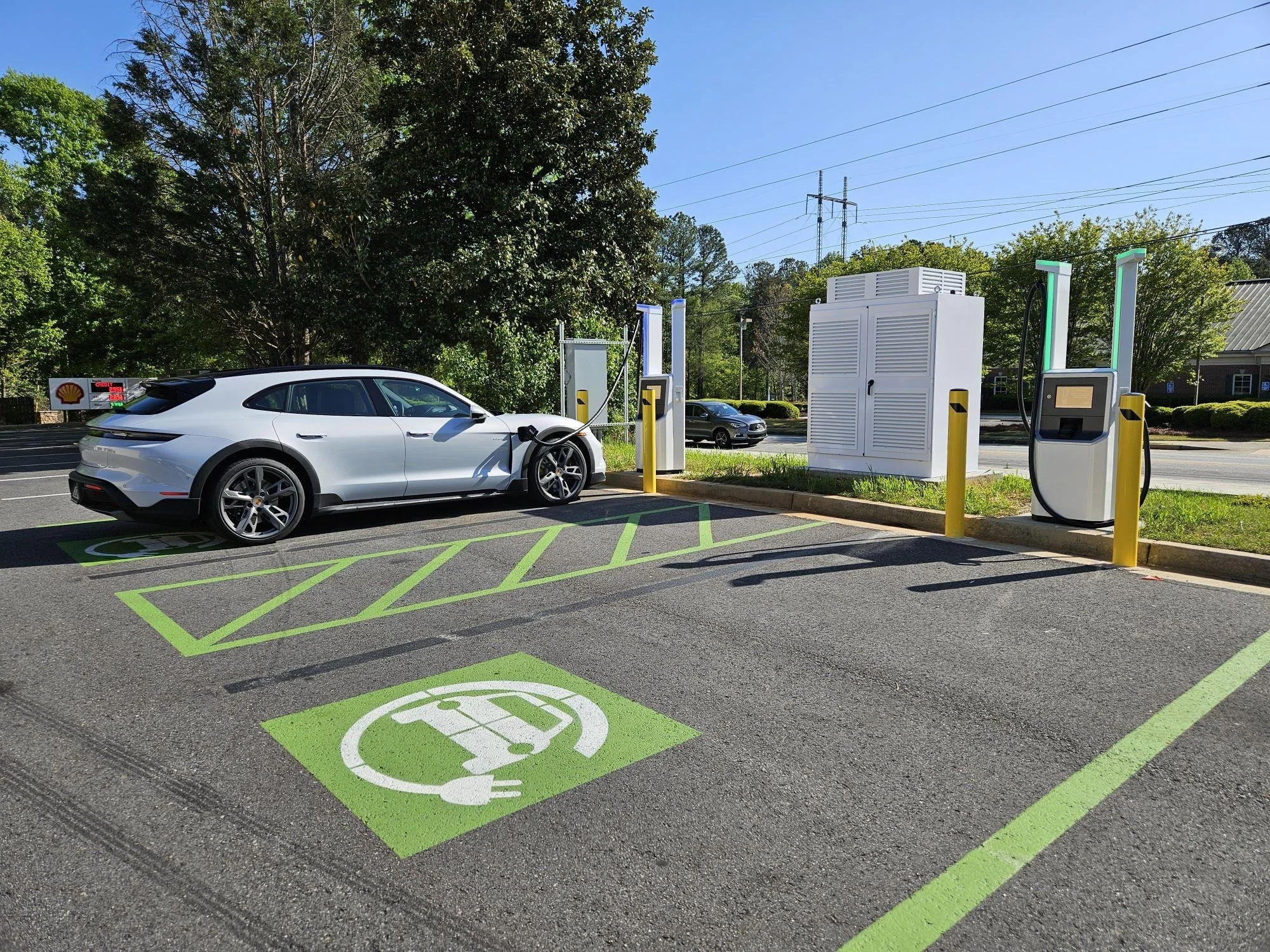 An electric vehicle charging station with a white car plugged into an electric charger. The designated parking spot has green lines and a symbol indicating it is reserved for electric vehicles.