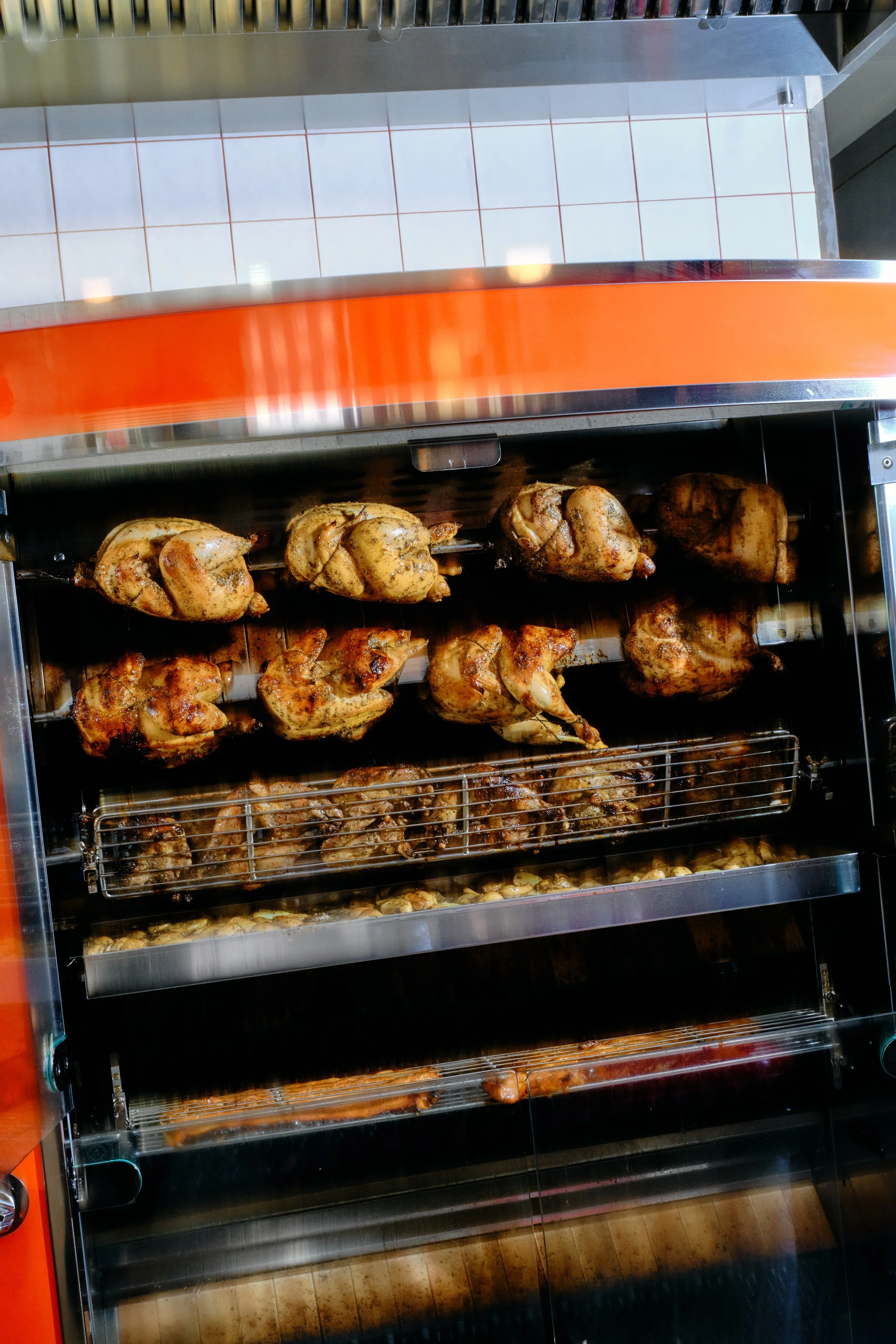 Poulets rôtis dans une rôtissoire à gaz orange vif, cuits à la broche dans une cuisine commerciale.