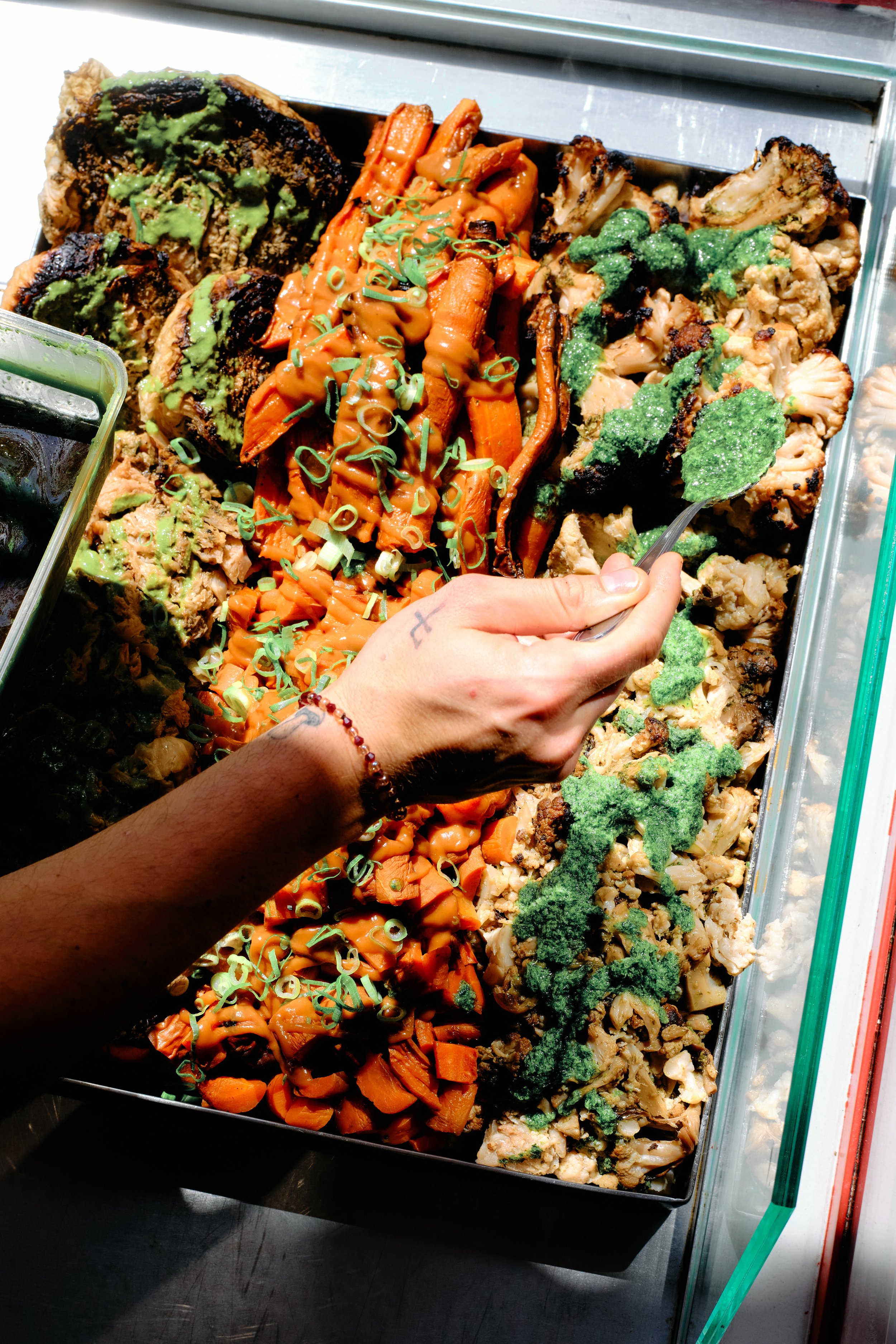 Un plateau de nourriture végétarienne contenant différentes sortes de légumes rôtis, garnis de sauces et d'herbes, présenté dans un plat en métal