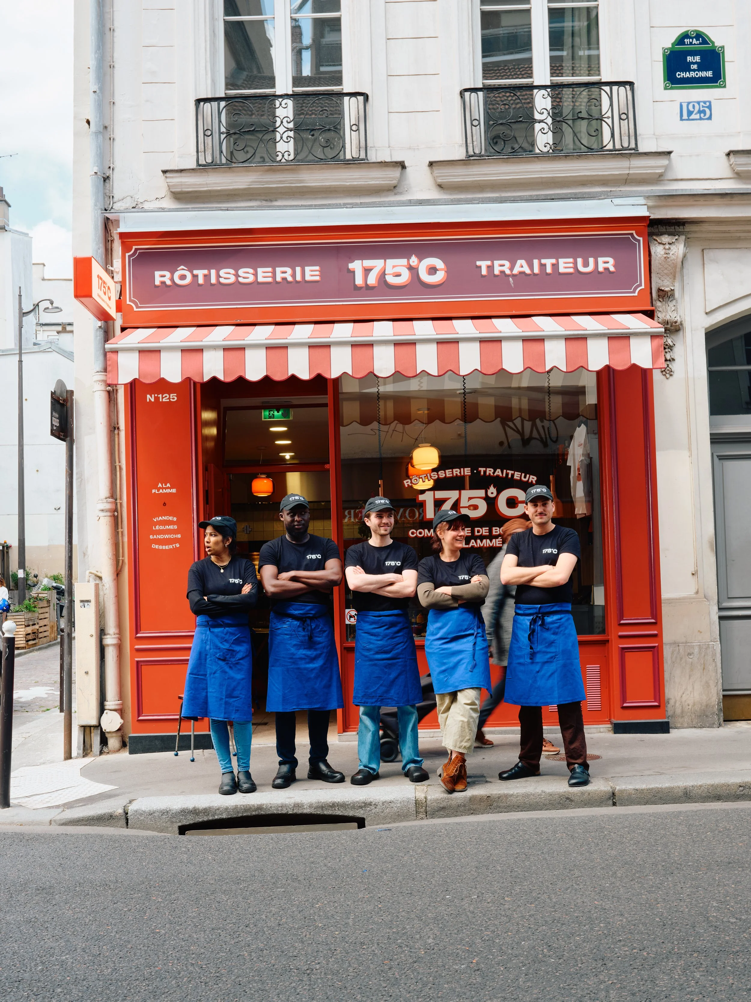 Groupe de cinq personnes posant devant une devanture de restaurant rouge avec un enseigne indiquant 175°C, spécialisé en rôtisserie et traiteur, à Paris, avec des vêtements de travail bleus et des casquettes.