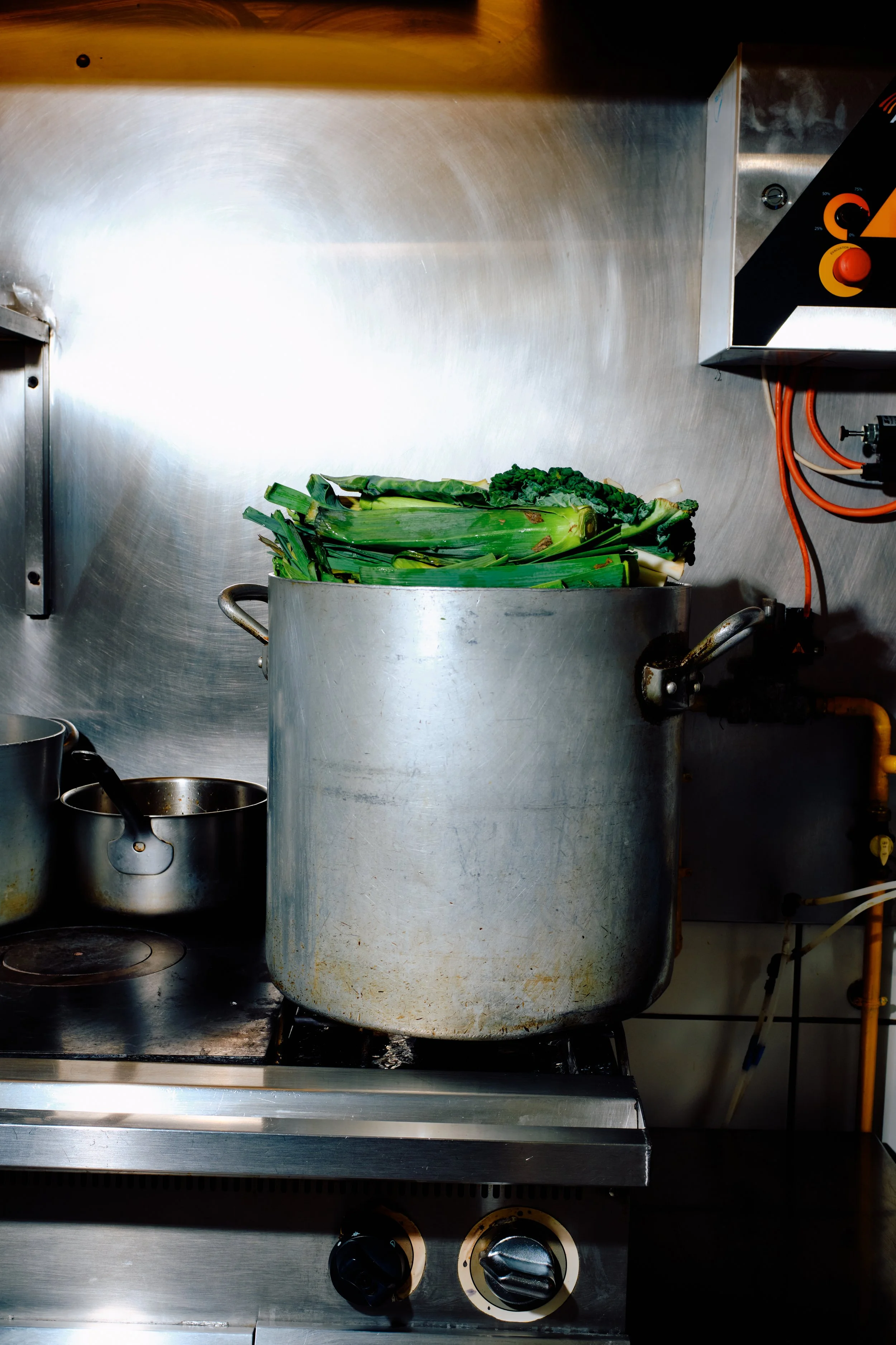Casserole en métal contenant des légumes verts, notamment du céleri, situé sur une cuisinière en acier inoxydable dans une cuisine industrielle.
