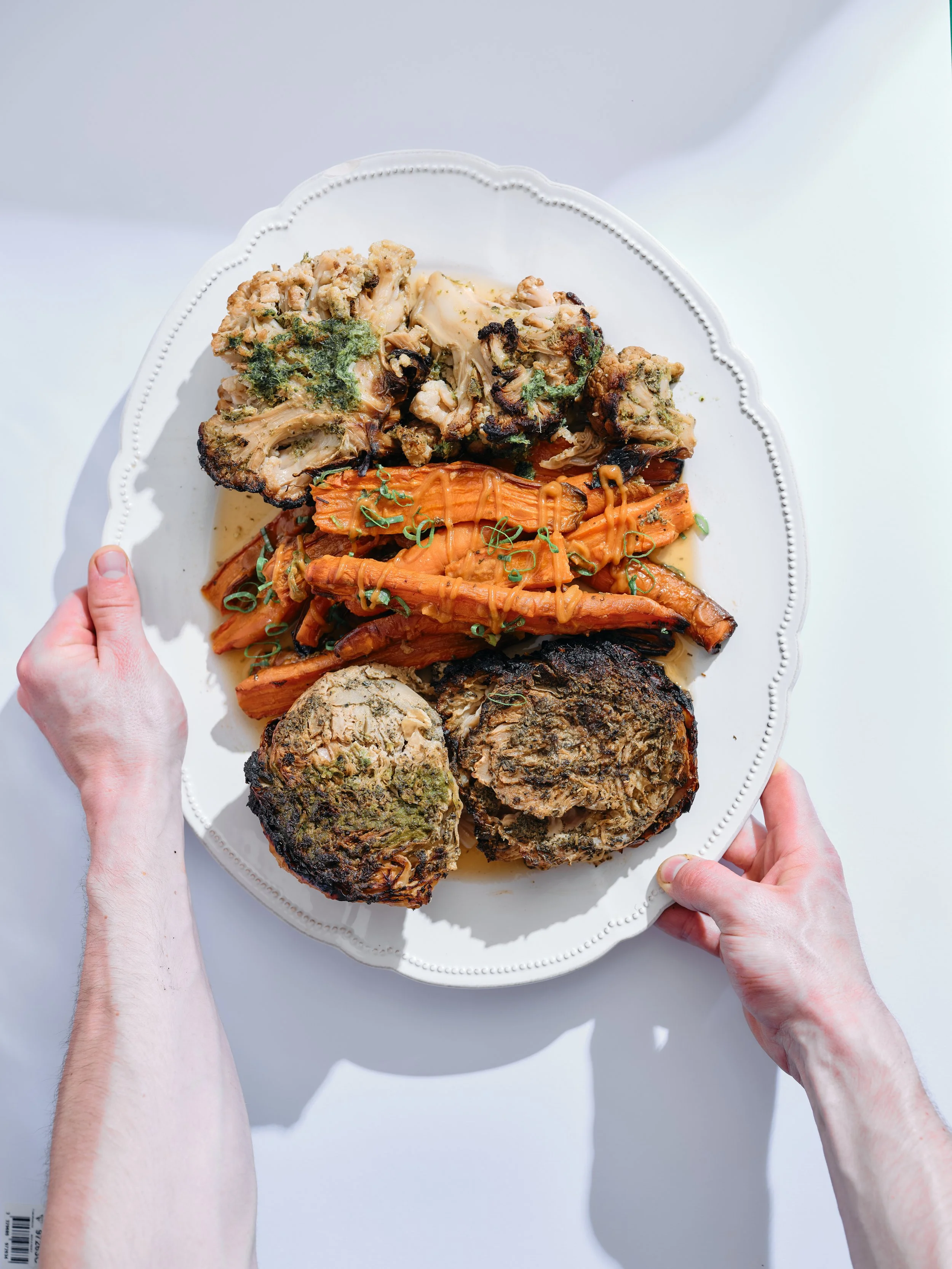 Assiette blanche avec morceaux de viande d'agneau rôtie, racines de carotte, et un plat de viande hachée avec des herbes