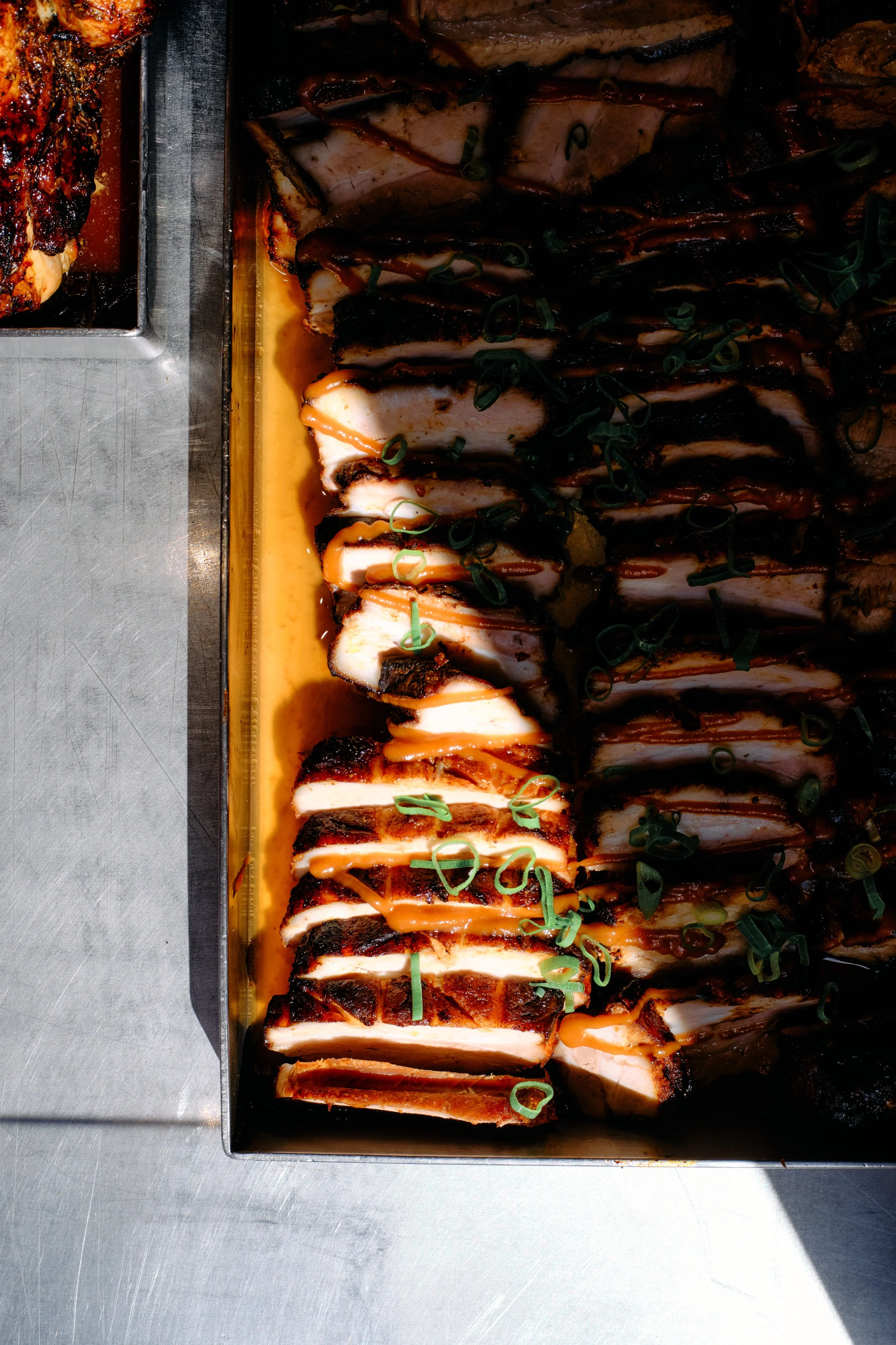 Gros plan de tranches de rôti de porc grillé garni de sauce, de ciboulette hachée et de sauce moutarde, présenté dans une plaque de cuisson