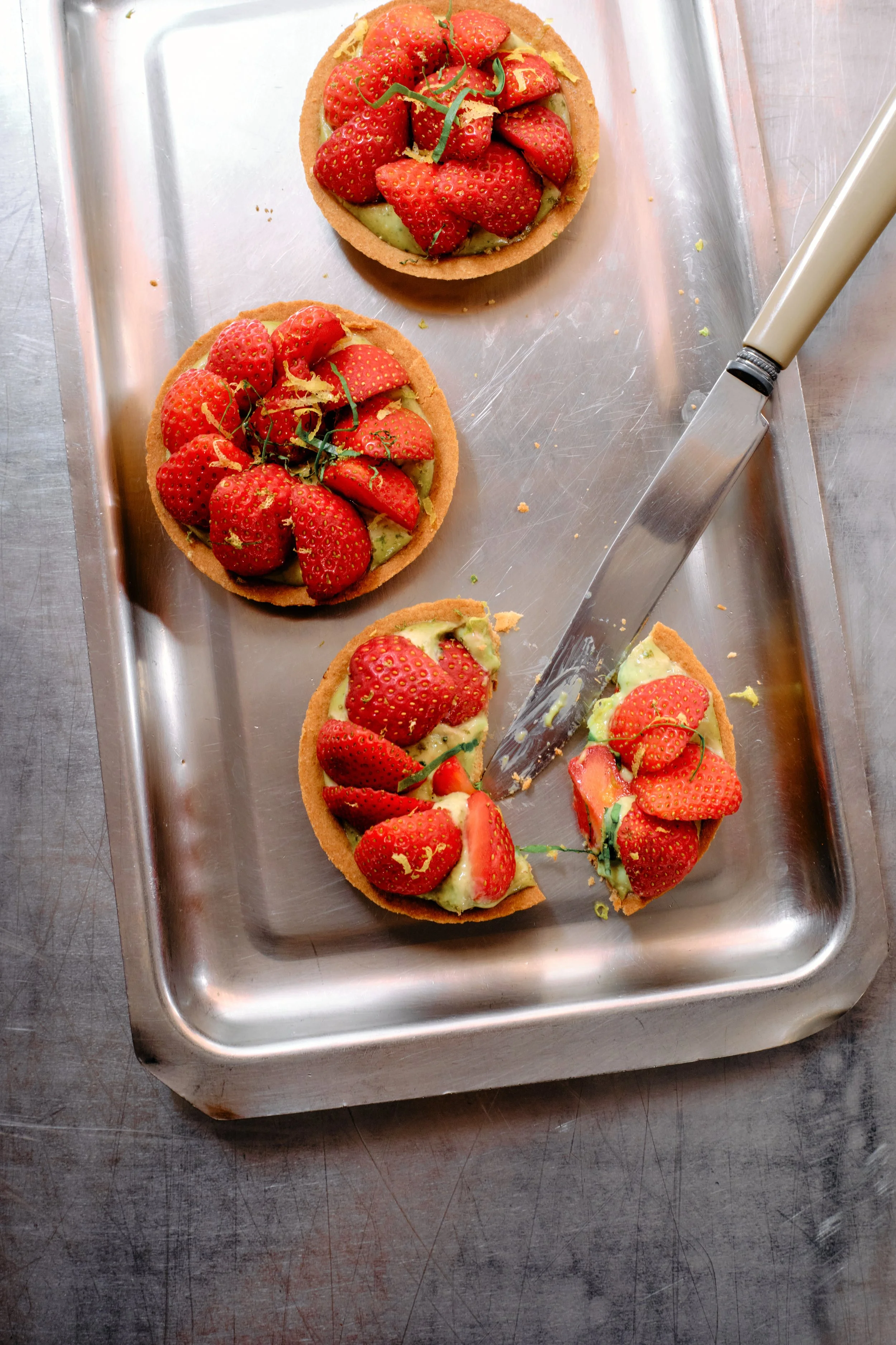 Tartelettes aux fraises sur une plaque en métal, un couteau à pâtisserie posé à côté.