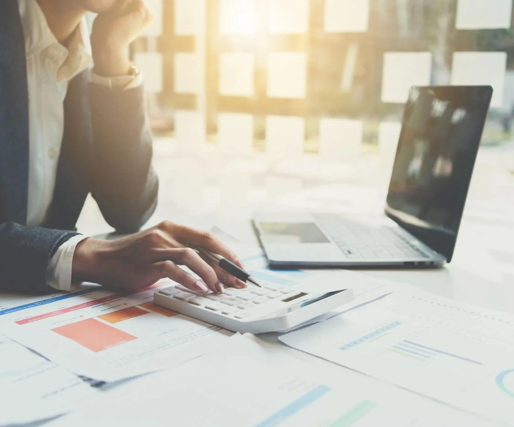 Small business owner reviewing financial reports and using a calculator to manage cash flow in Iredell County North Carolina