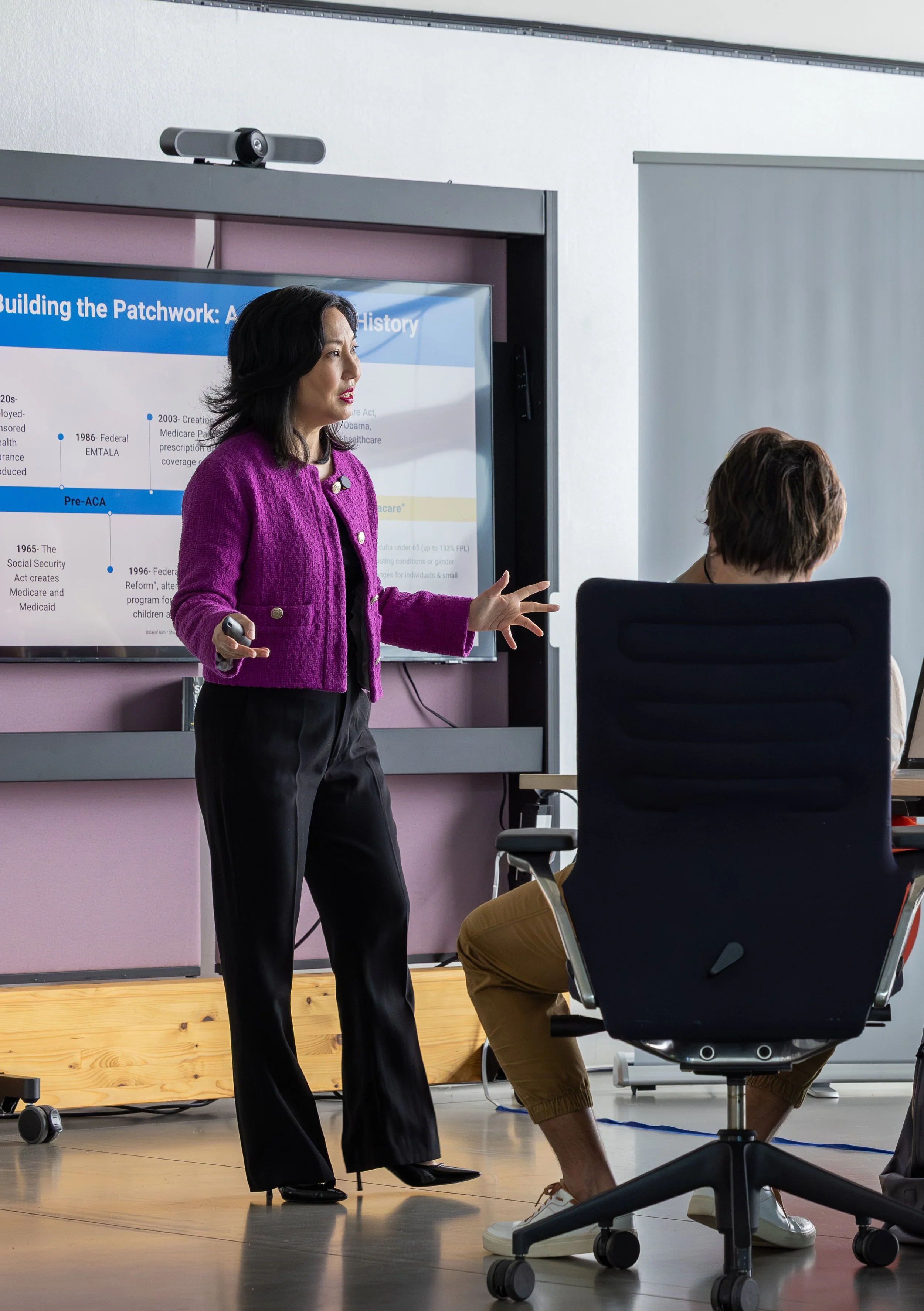 Carol Kim in a purple blazer giving a healthcare presentation to a startup accelerator cohort.
