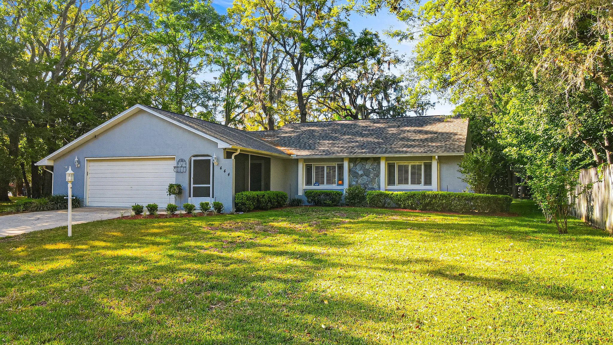 Front view of a single-story house with a gray facade, attached garage, green lawn, and trees in the background.