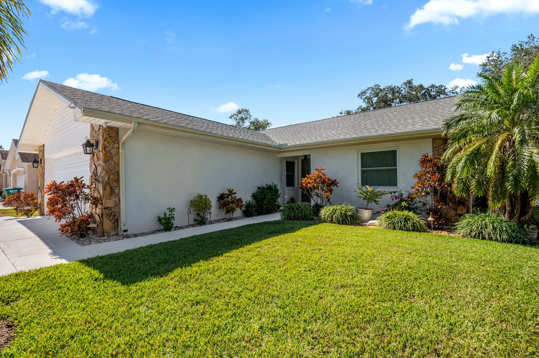 Front yard of a house with a well-maintained lawn, colorful bushes, and a palm tree on the right side under a clear blue sky.