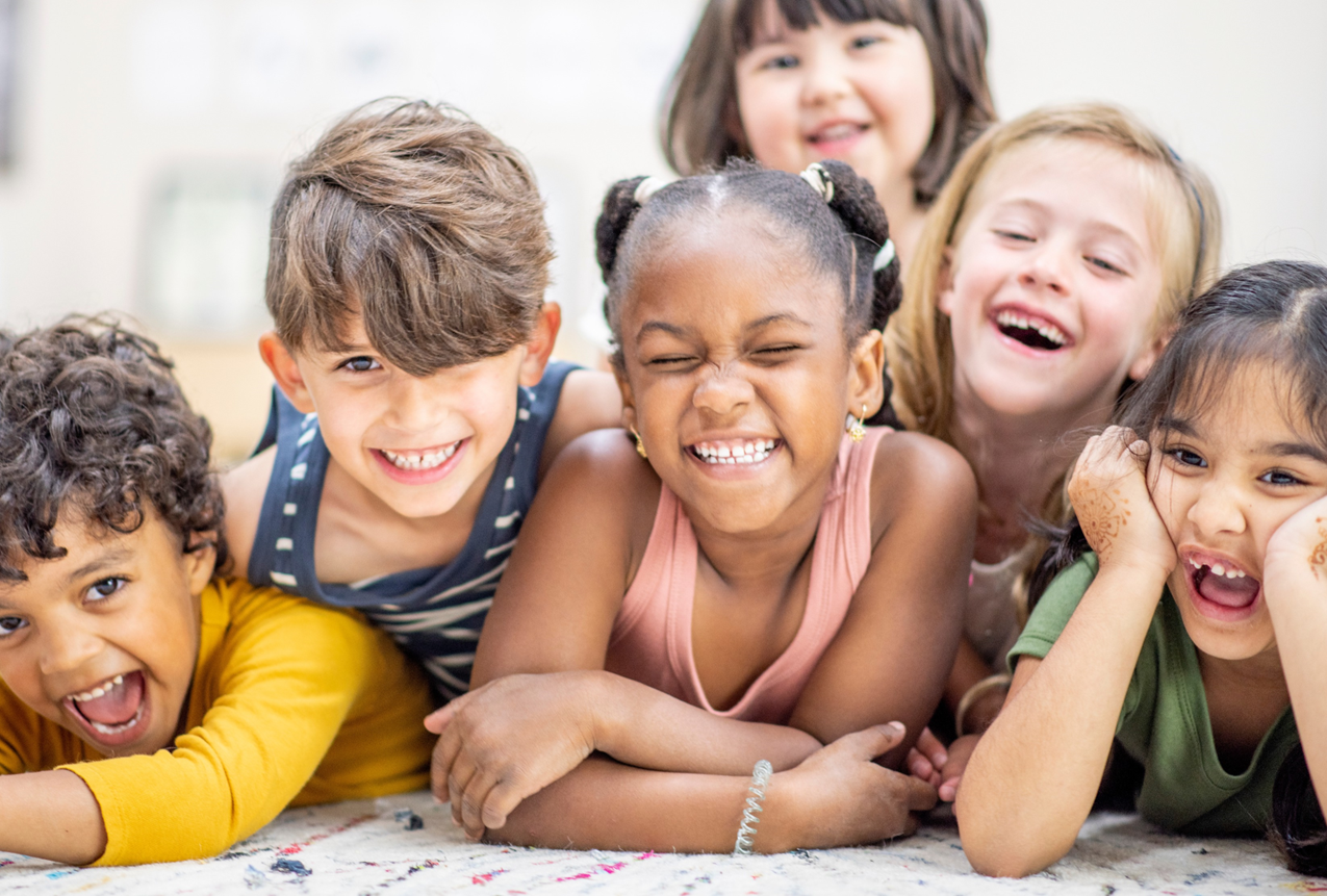 Group of six diverse children lying on the floor, smiling and laughing together.