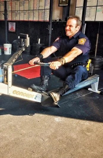 A man in a police uniform using a rowing machine in a gym or fitness area.
