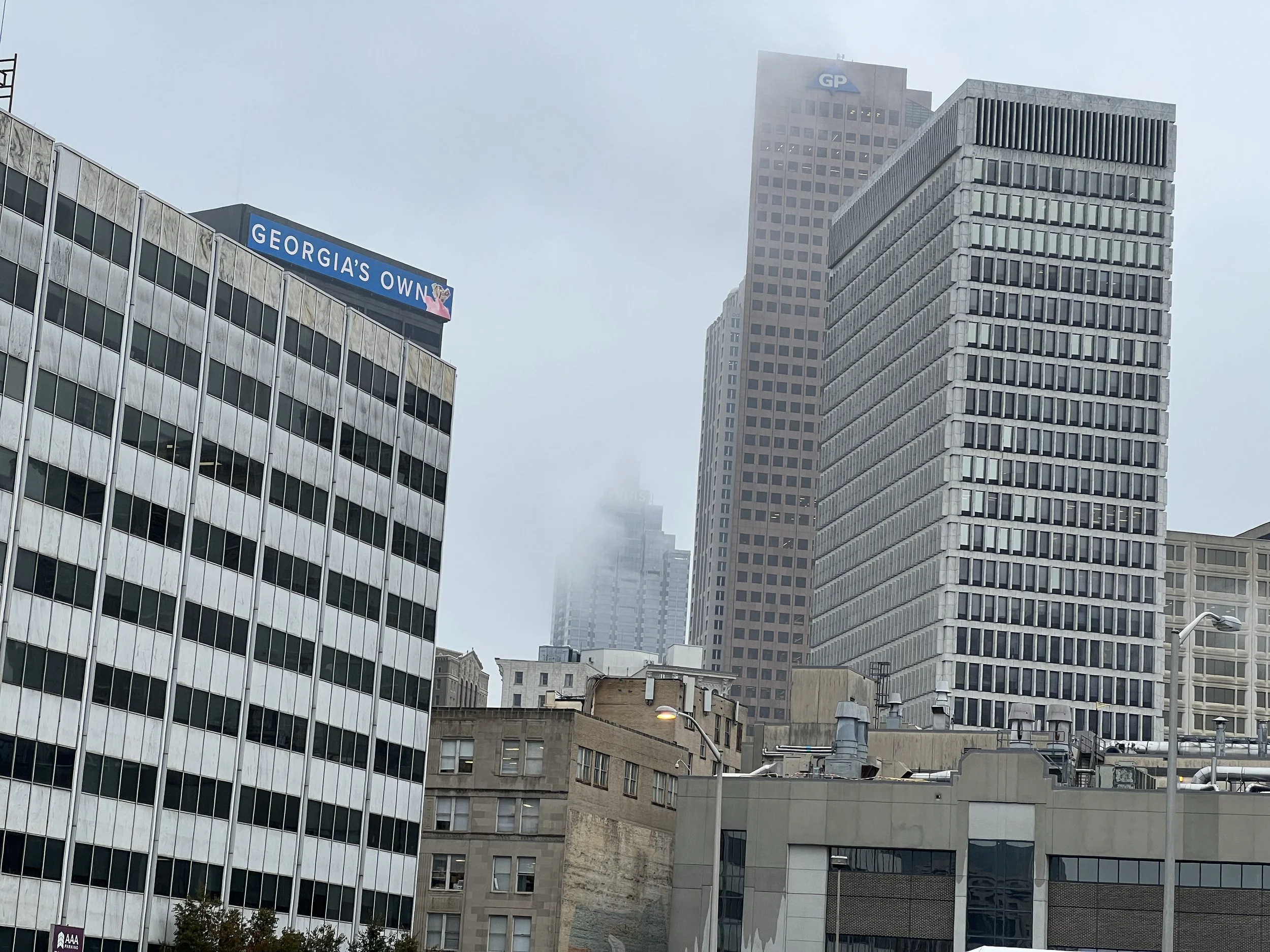 Cityscape of tall office buildings in foggy weather, with a visible sign that reads 'GEORGIA'S OWN' on one of the buildings.