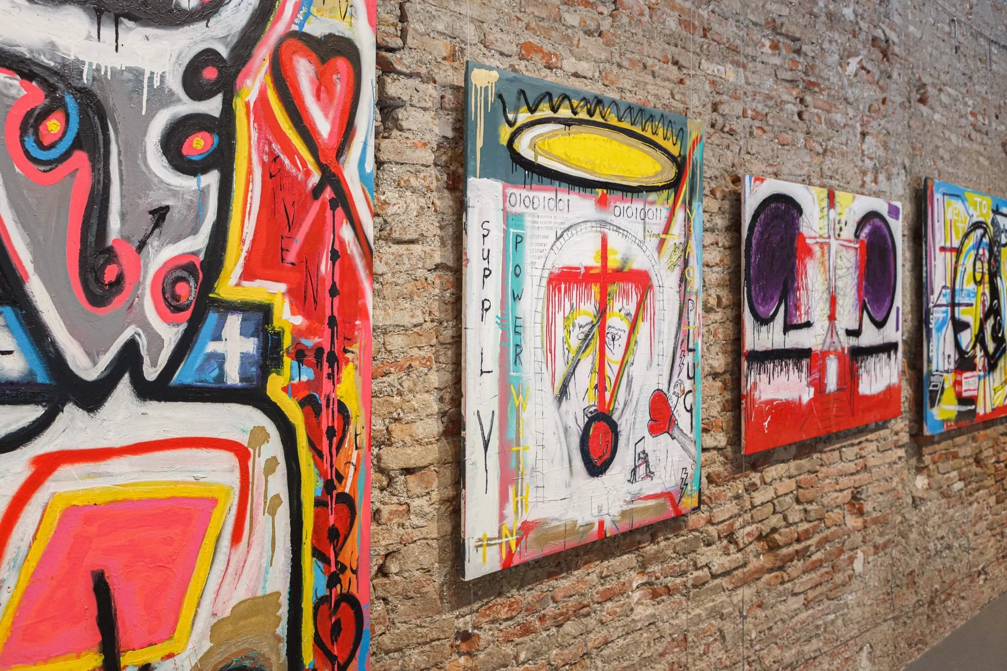 Angled installation view of PIGSY paintings hung on brick wall, showing depth and sequencing of works at La Casa Amarilla Malaga