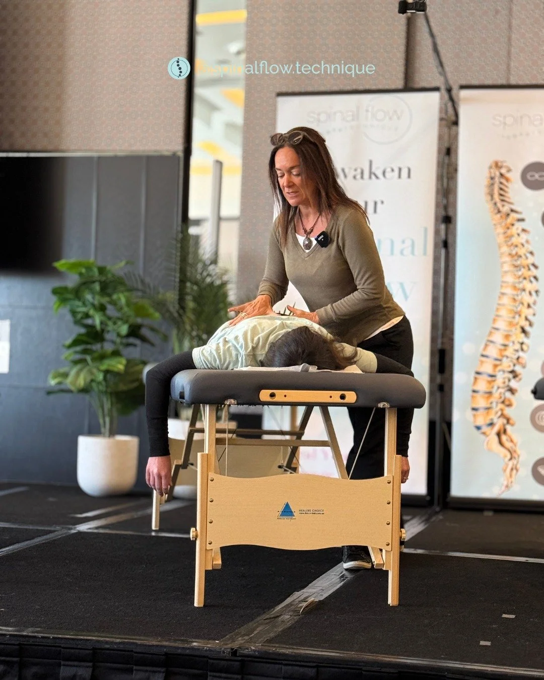 Jayne Birkett demonstrating Spinal Flow Technique next to a nervous system and spinal health anatomical chart.