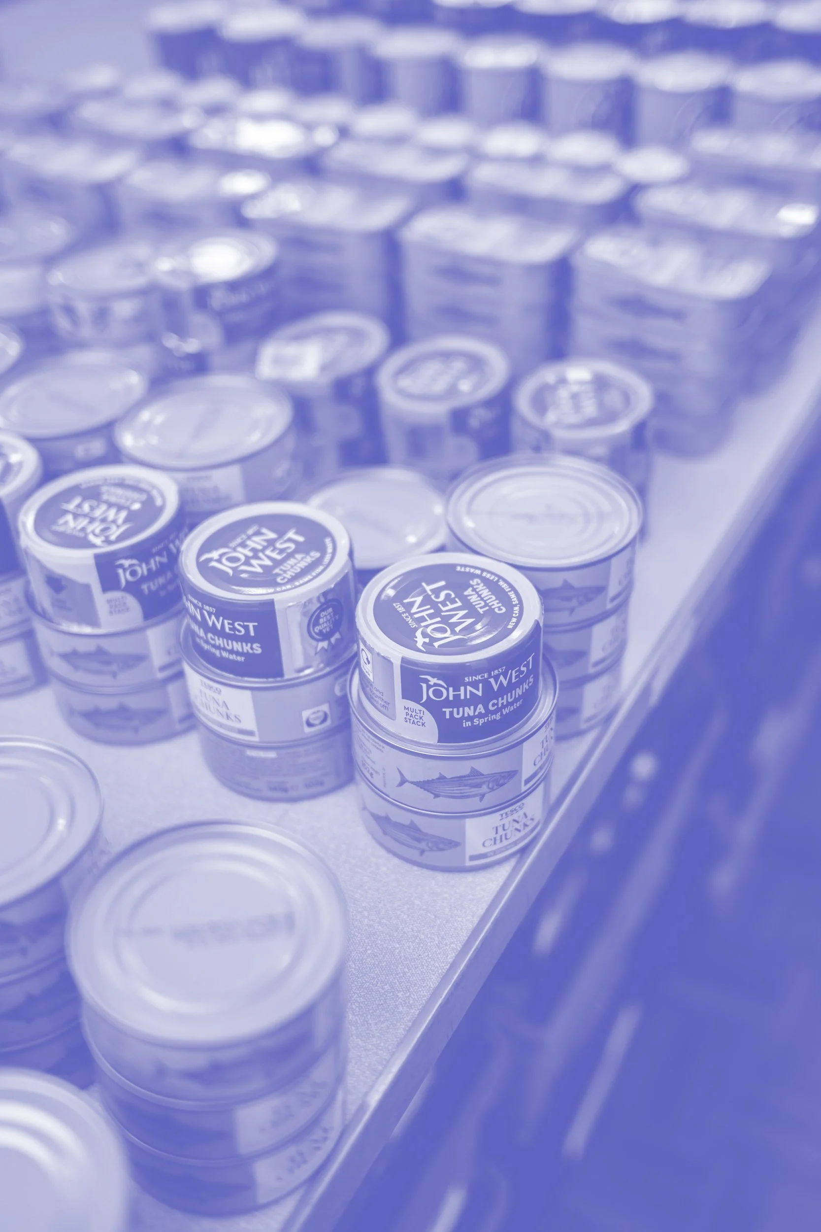 Cans of John West tuna stacked on a store shelf.