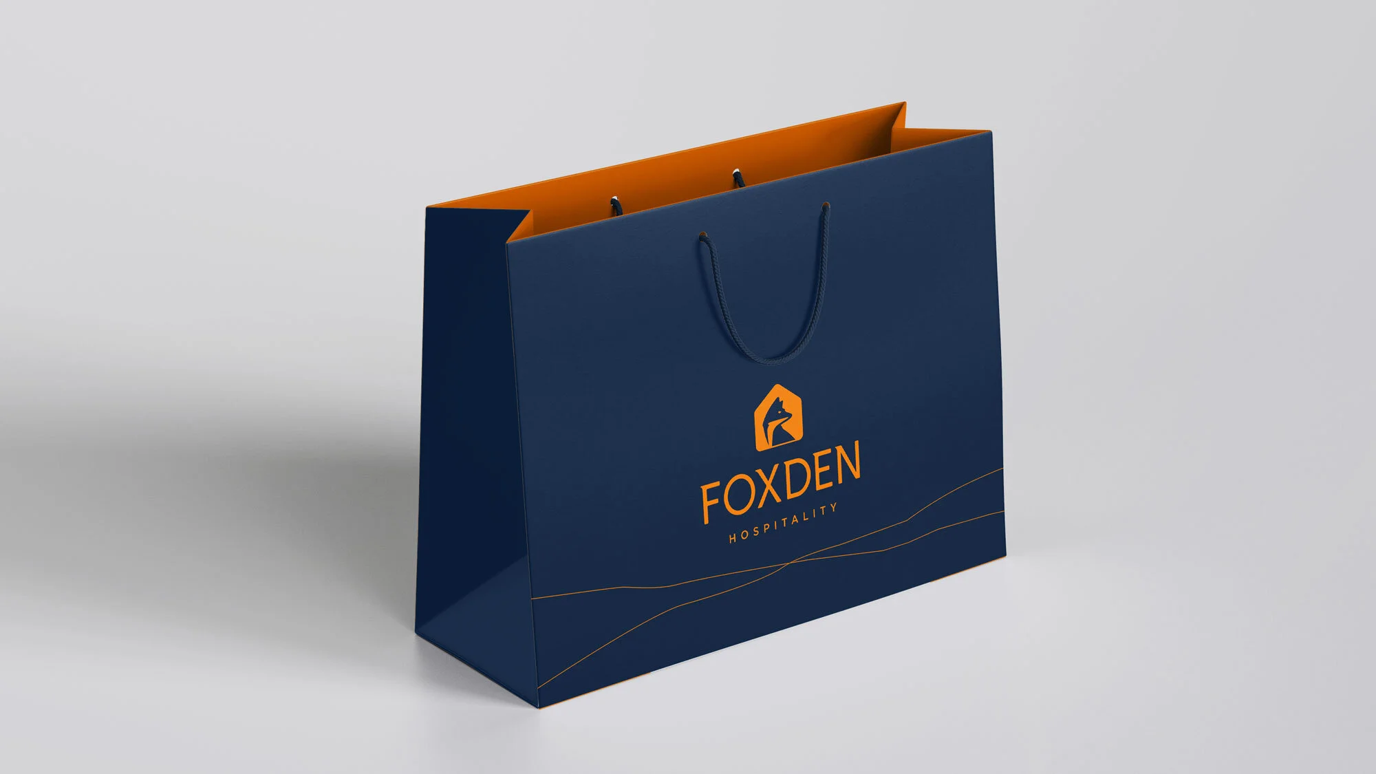 A navy blue shopping bag with orange interior and handles, featuring a fox logo and the words 'FOXDEN HOSPITALITY' printed in orange.