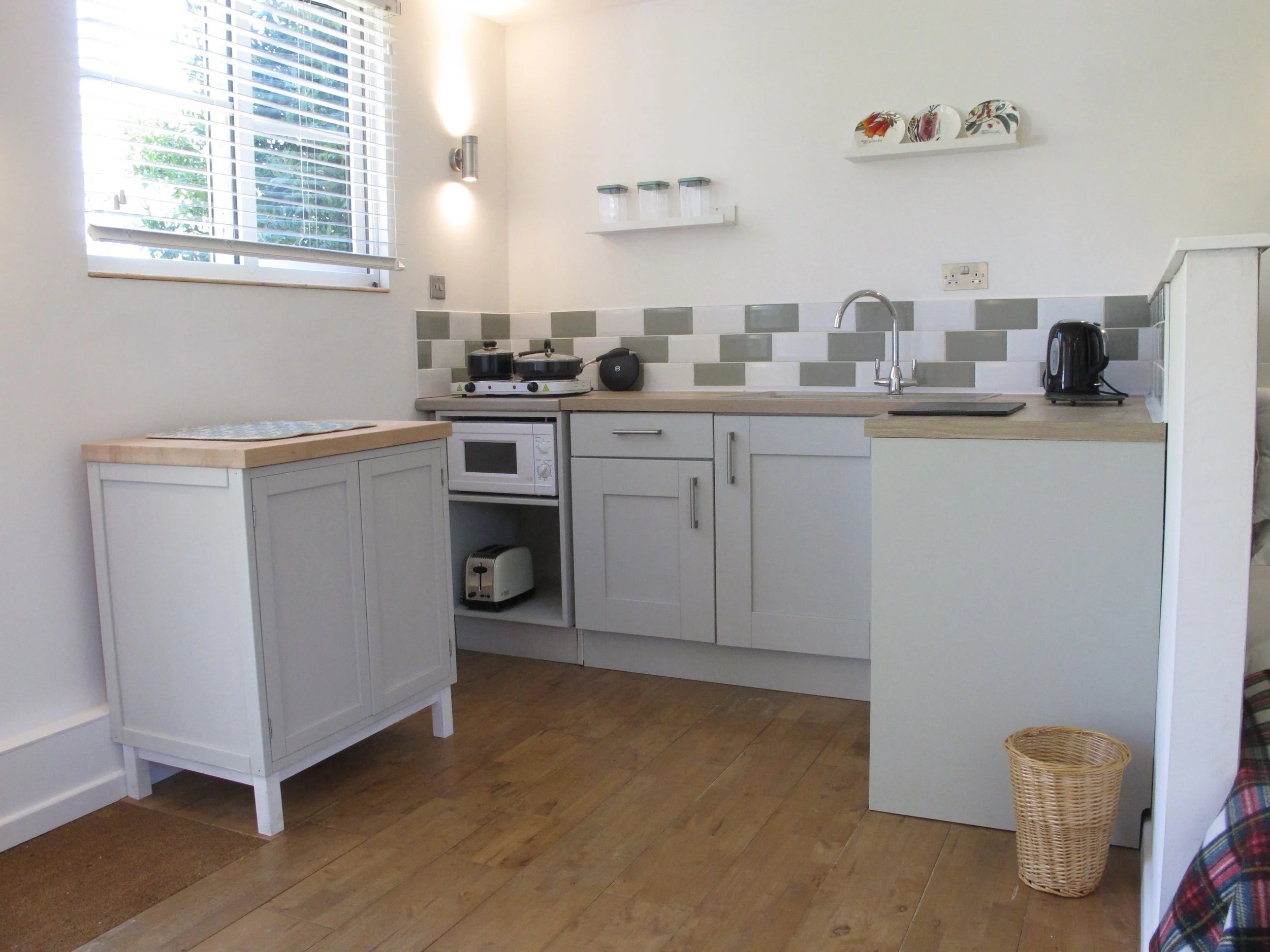 Compact kitchenette in a New Forest self-catering cabin featuring sink, draining board, kettle, a small hob, and a microwave.