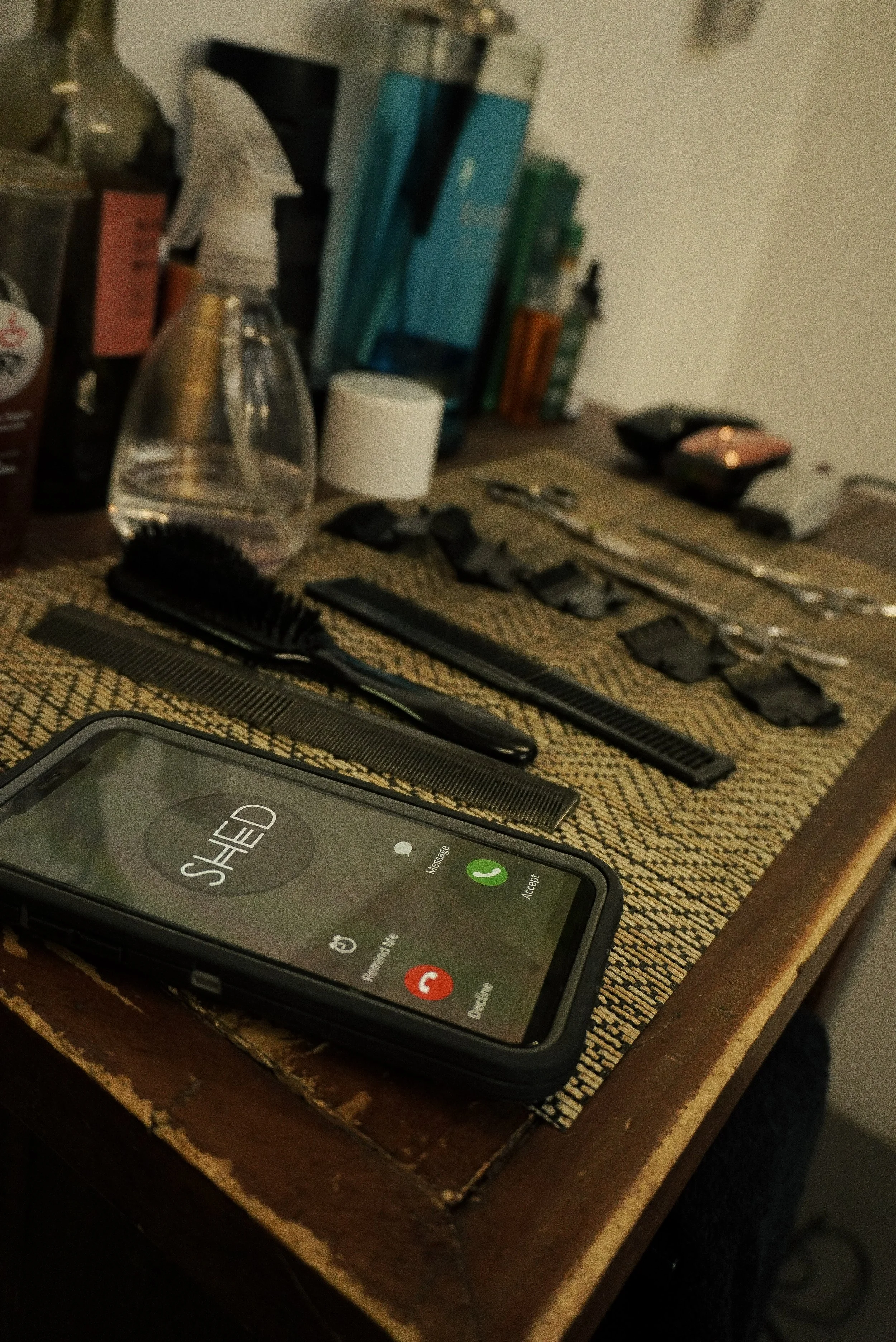A table with hair styling tools, including combs, scissors, and clippers, alongside a smartphone displaying an incoming call from an unknown contact.
