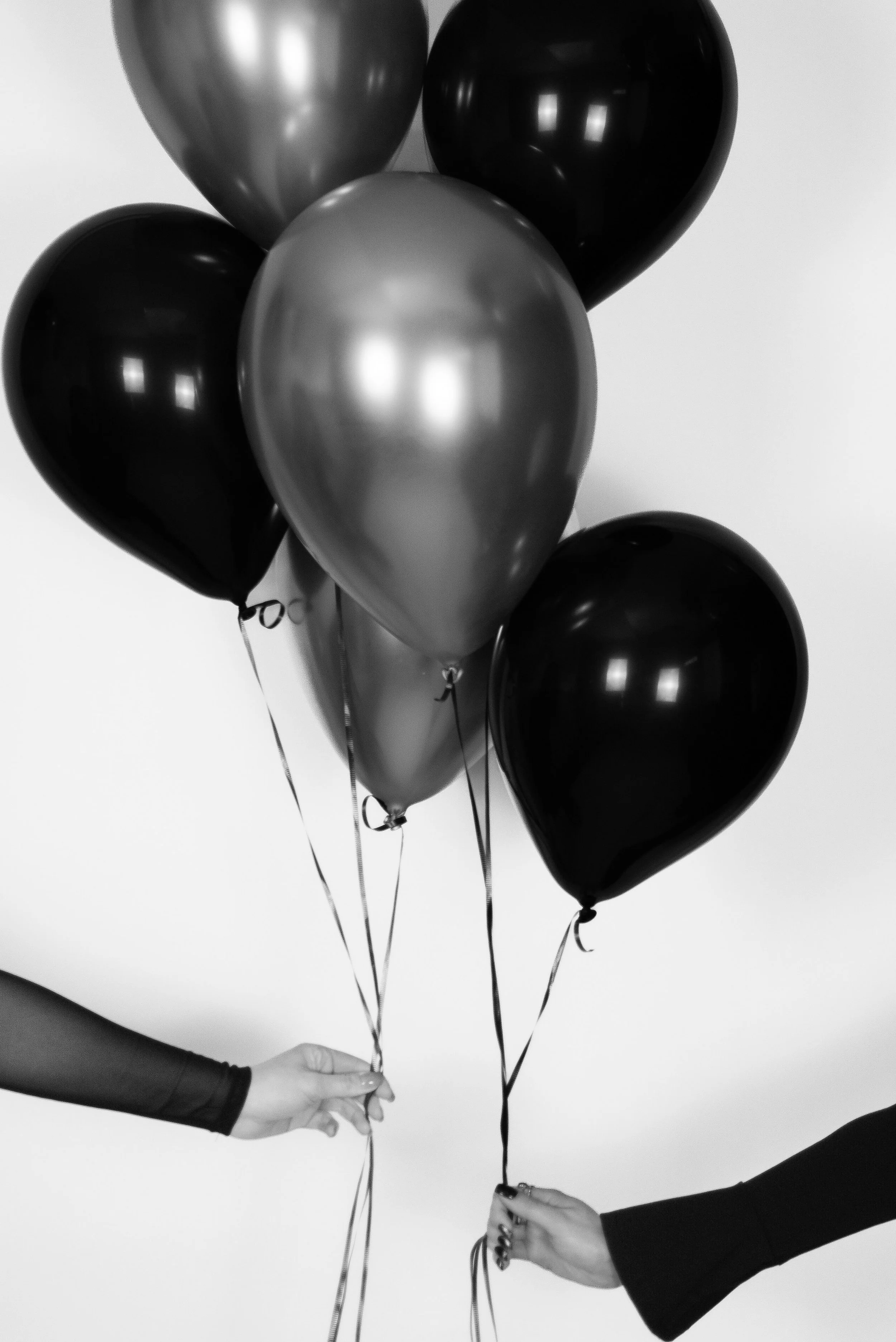 Black and silver balloons being held by two people against a white background.