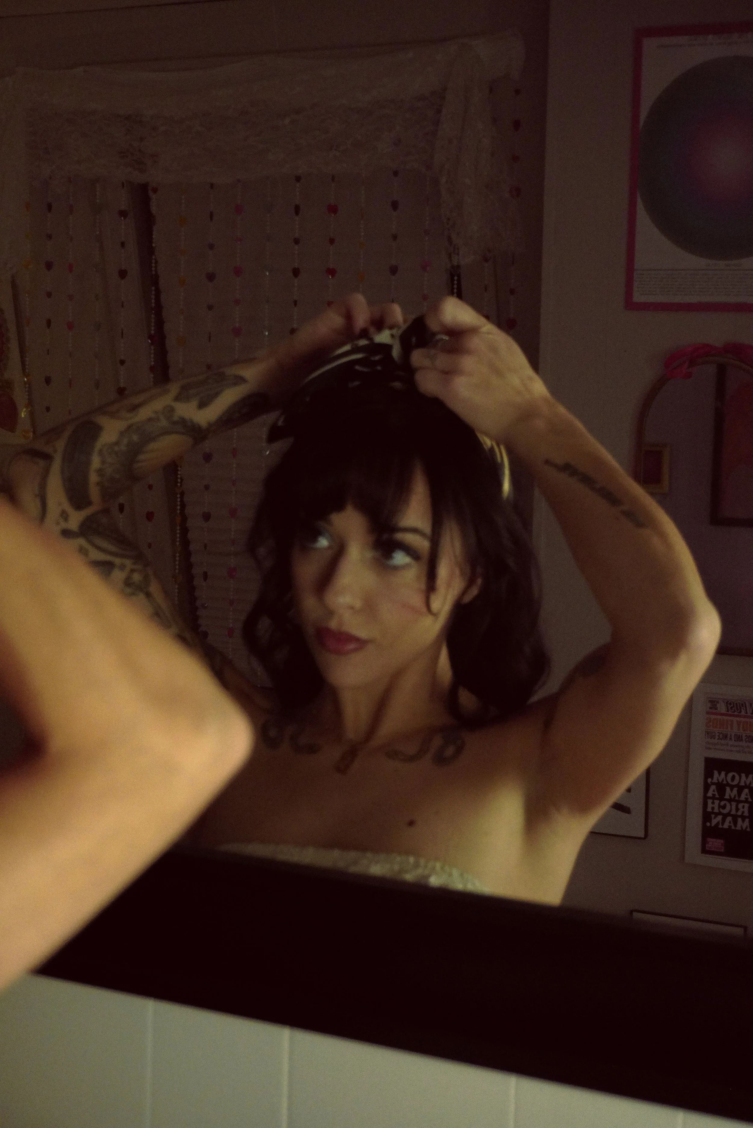 Woman with dark curly hair and tattoos adjusting her hair in front of a mirror.