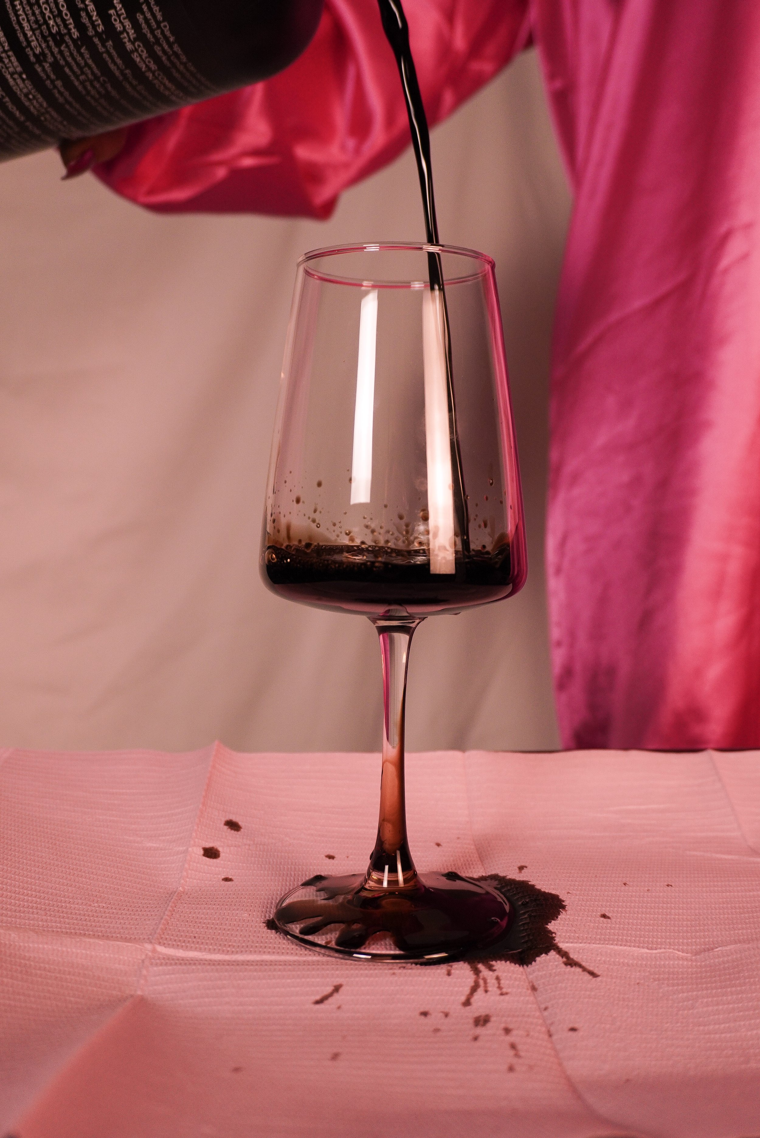 A glass of red wine being poured from a bottle onto a pink tablecloth.