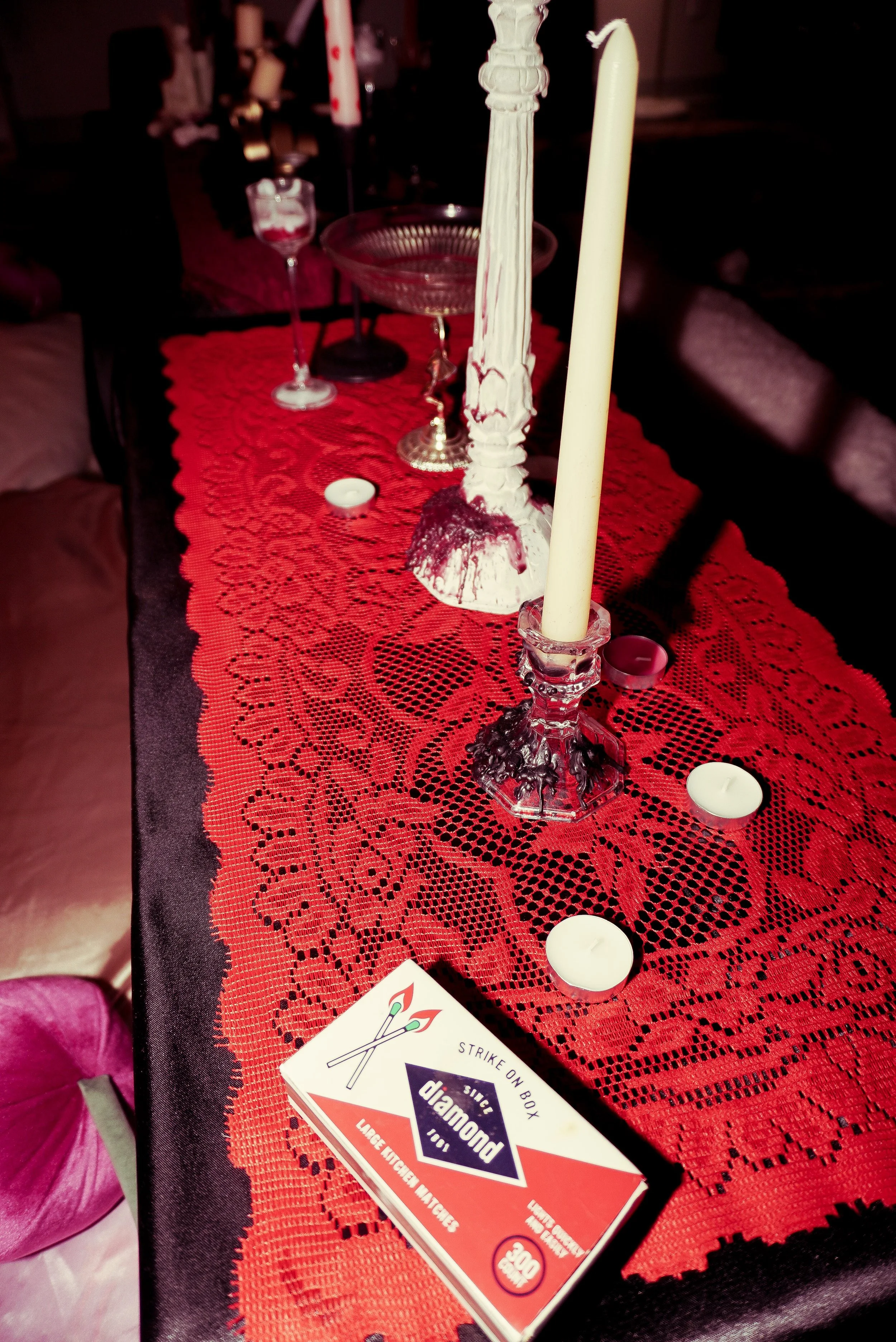 A dining table with a red lace table runner, candles, and matchbox with the text 'Strike on box, Diamond'.