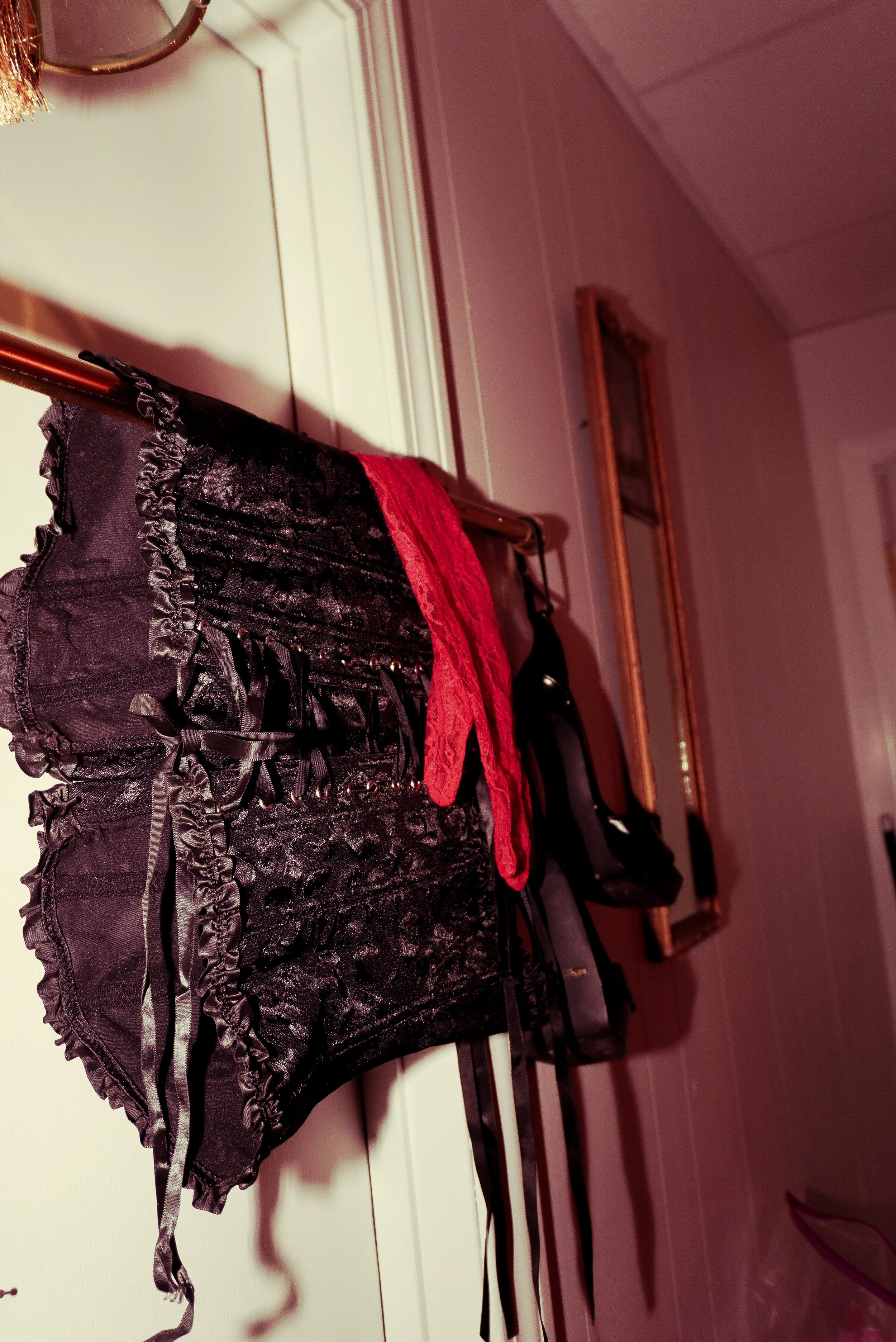 Black lace and satin lingerie with ruffles hanging on a clothes rack in a pink room.