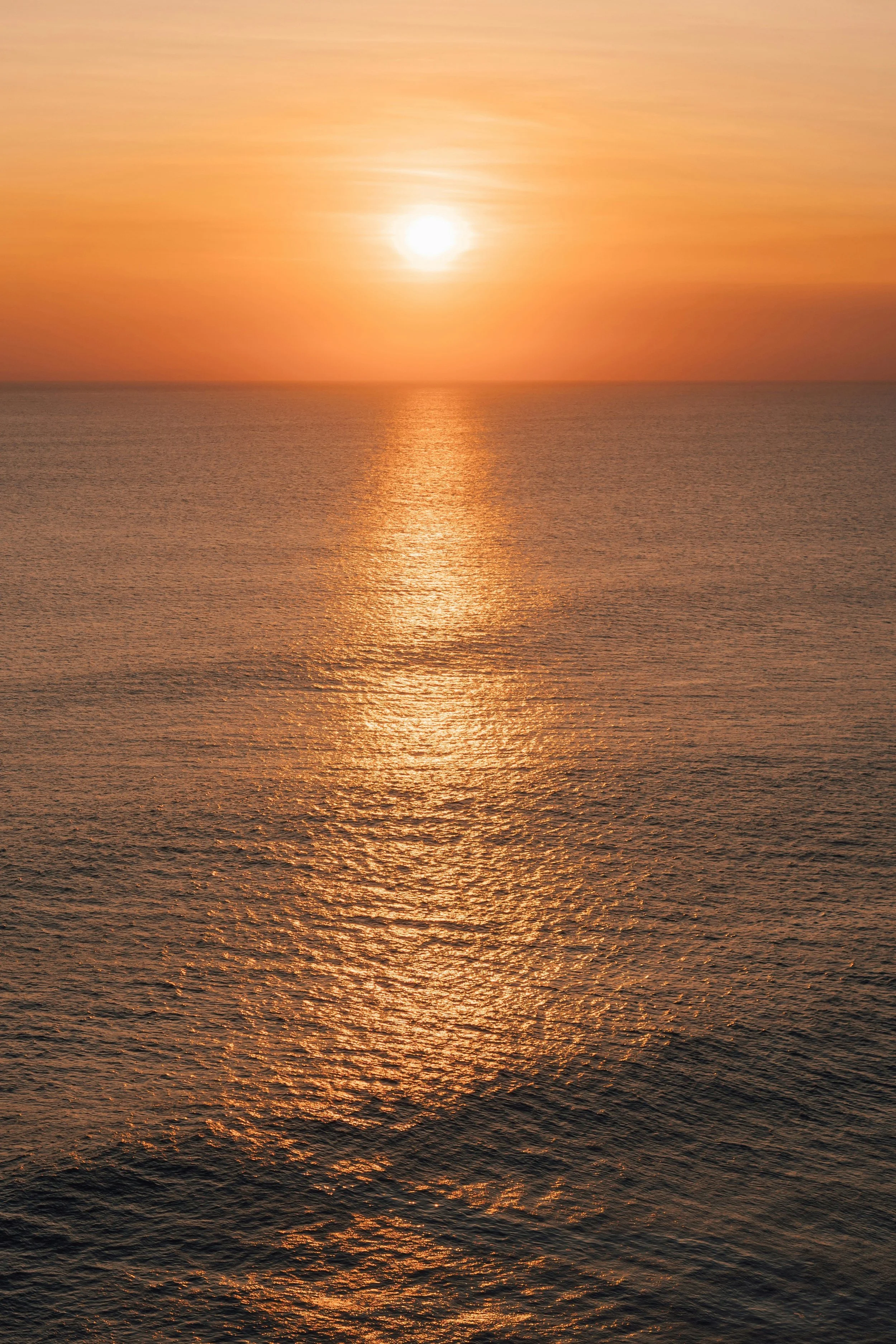 Sunset over the ocean with a reflection of the sun on the water.