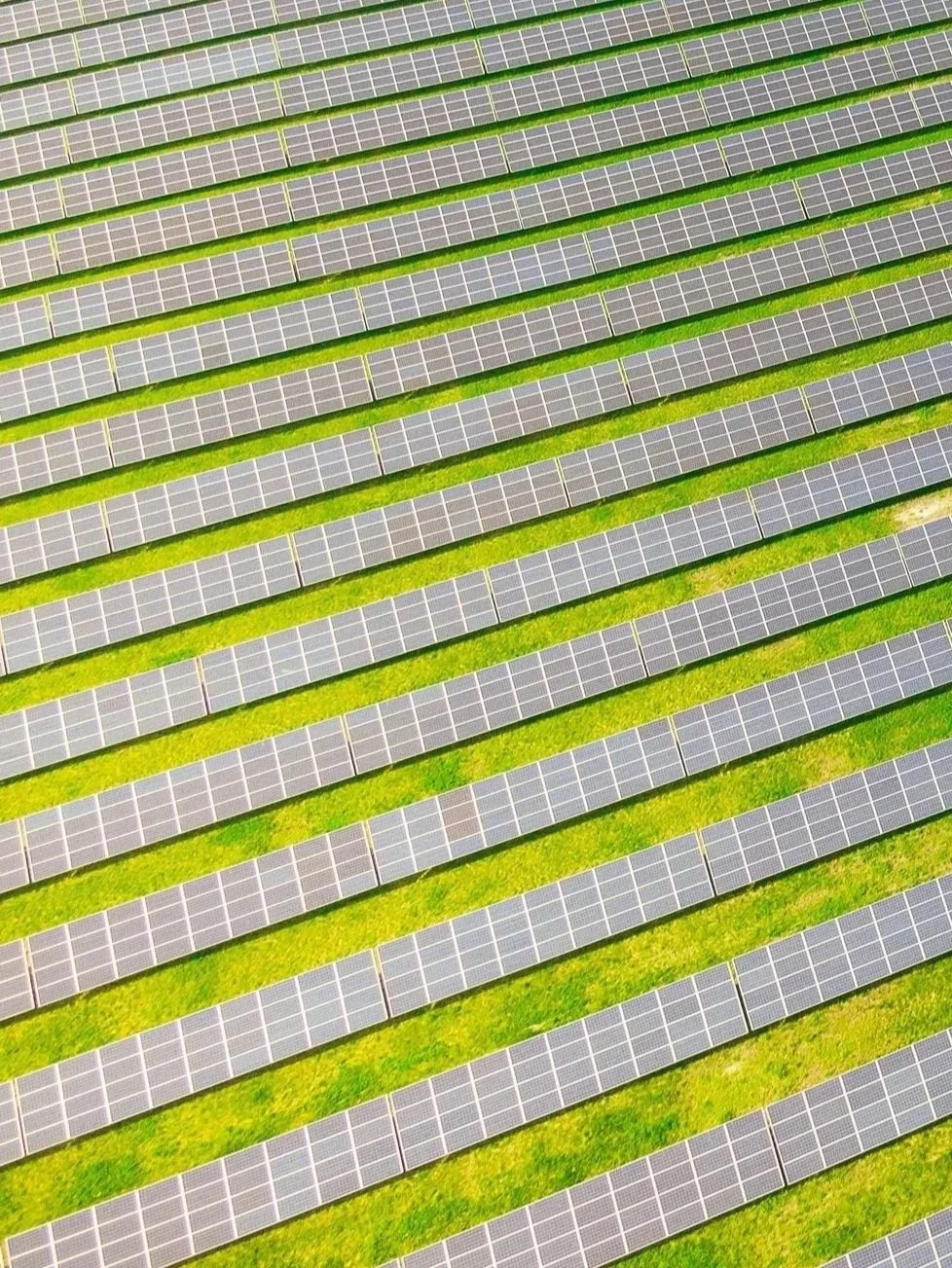 A bird's eye view of a large solar farm with rows of solar panels separated by green grass.
