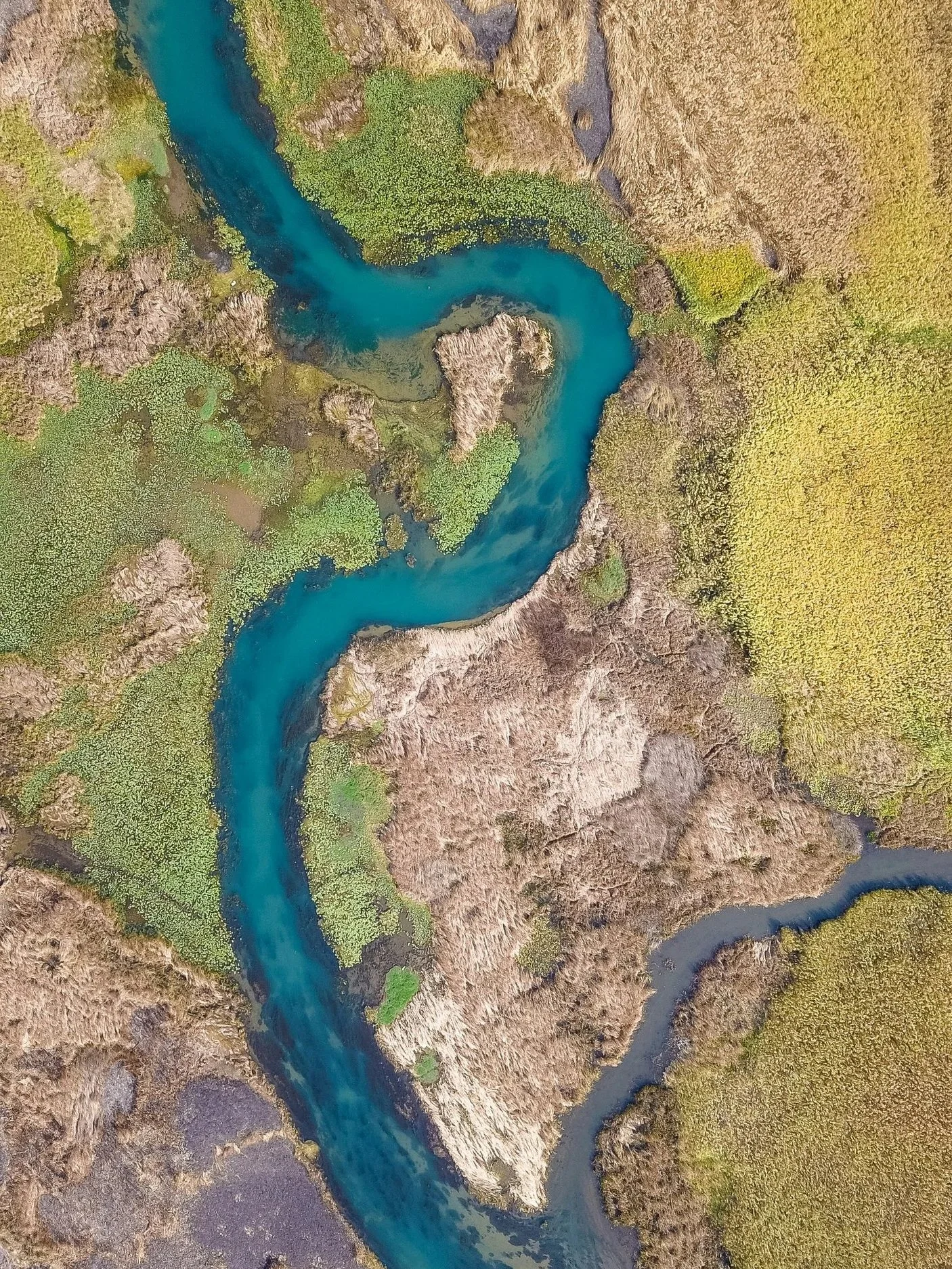 An aerial view of a winding river flowing through a landscape of scenic hills and green vegetation.