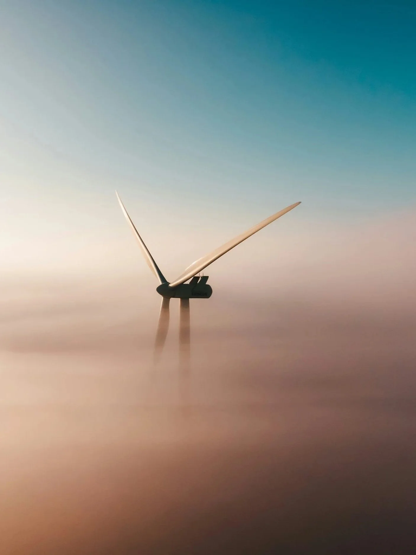 A wind turbine standing in a foggy landscape with a colorful sky in the background.