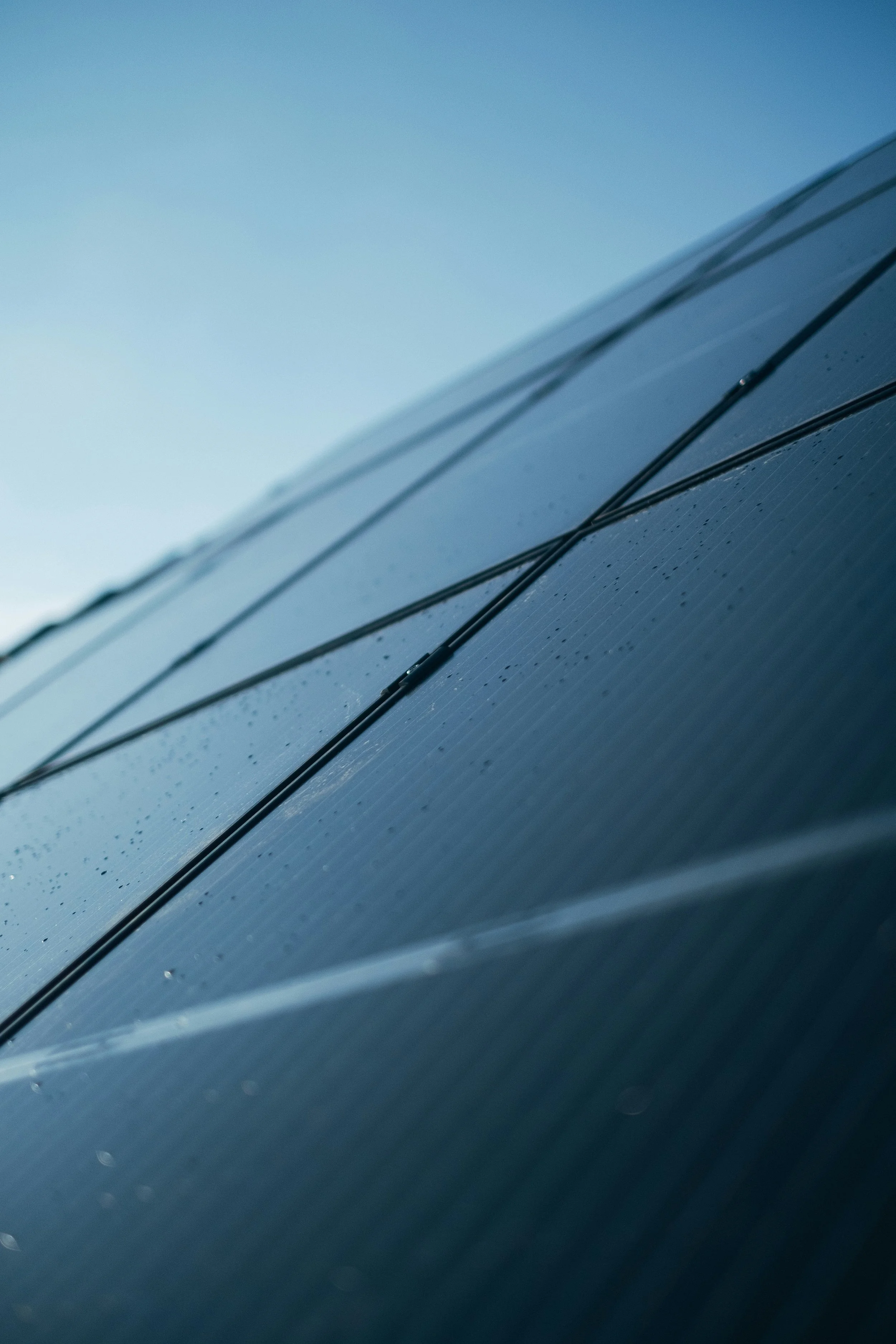 Close-up of solar panels with water droplets on their surface, set against a clear blue sky.