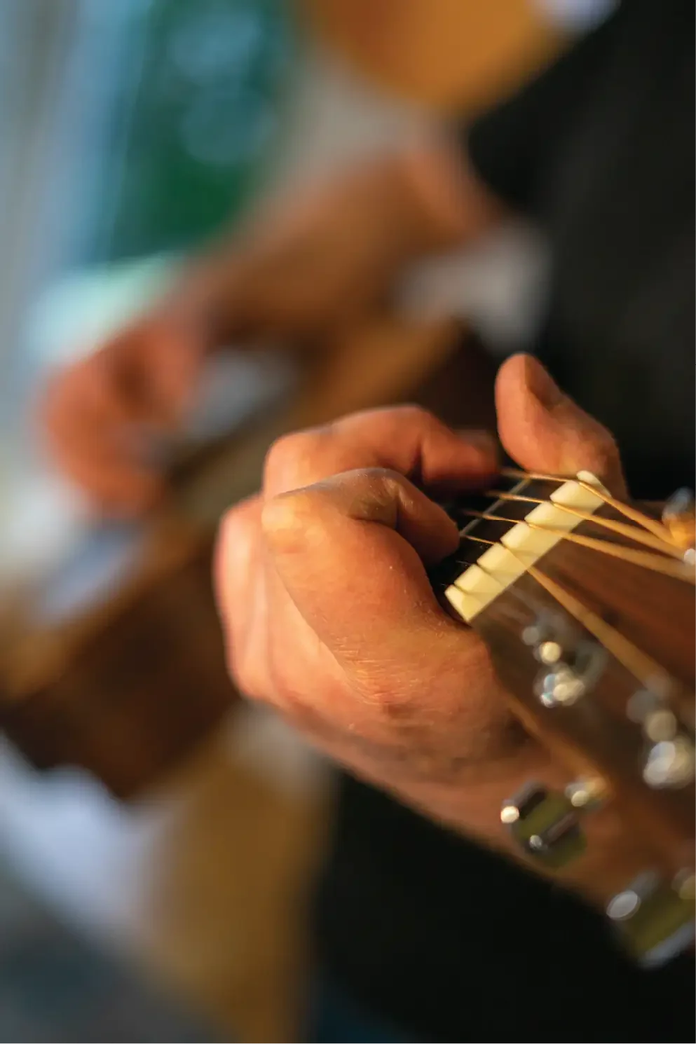 Close-up of a person's hand playing an acoustic guitar, with focus on the fretboard and fingers pressing the strings.