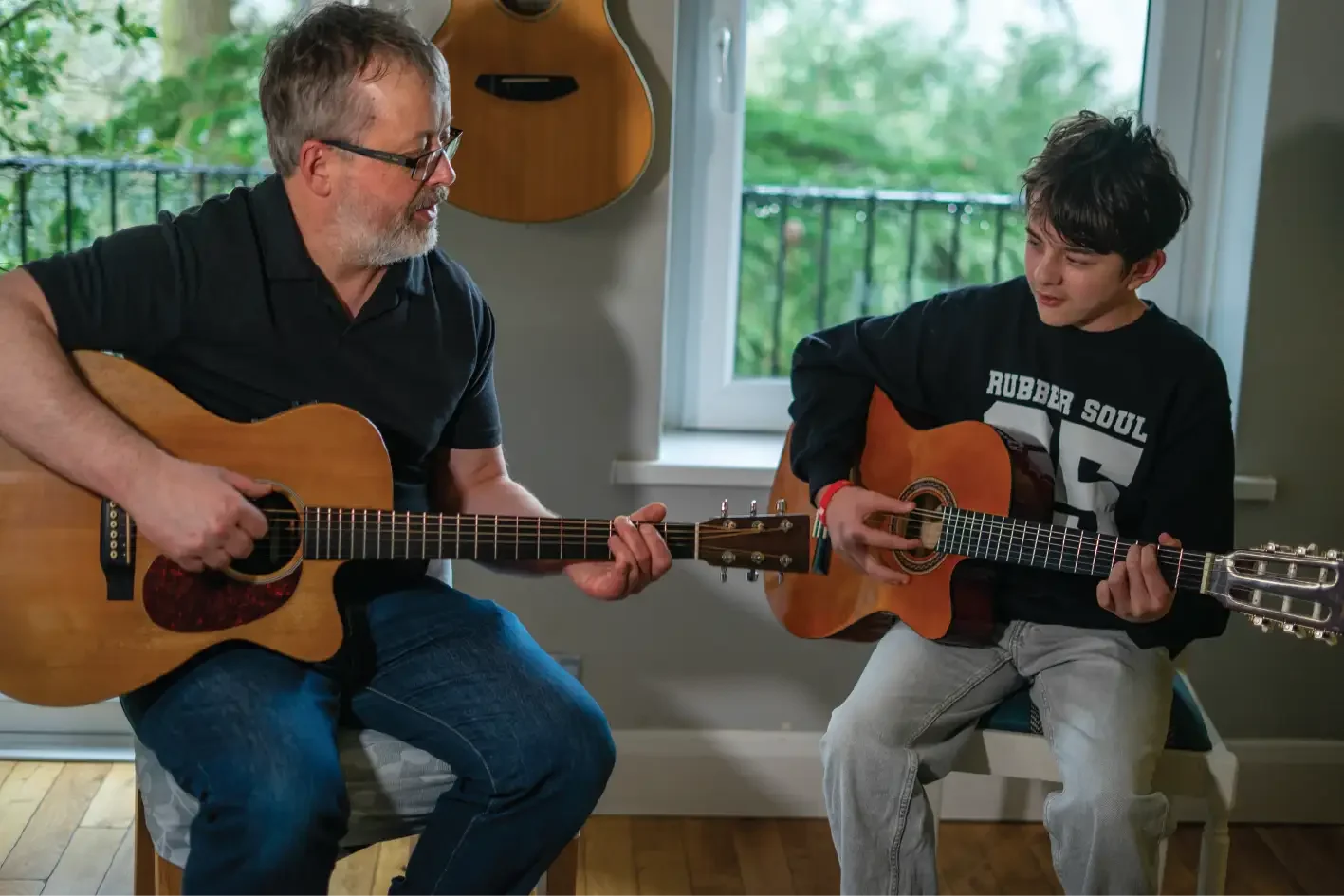 Guitar teacher and student sitting together playing acoustic guitars during a lesson