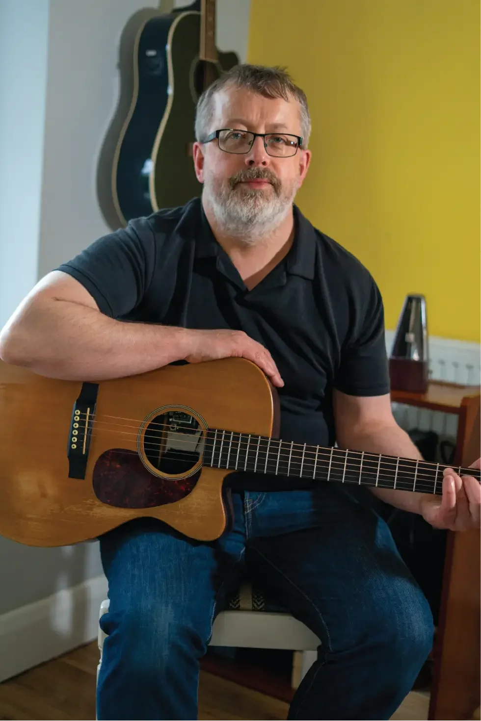 Guitar teacher sitting and holding an acoustic guitar, looking at the camera