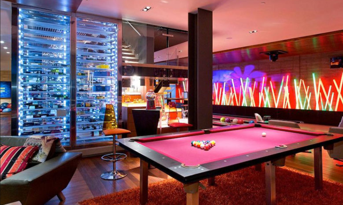 A pool table with a pink felt surface and billiard balls arranged on it, in a room with colorful neon lights and a wooden wall.