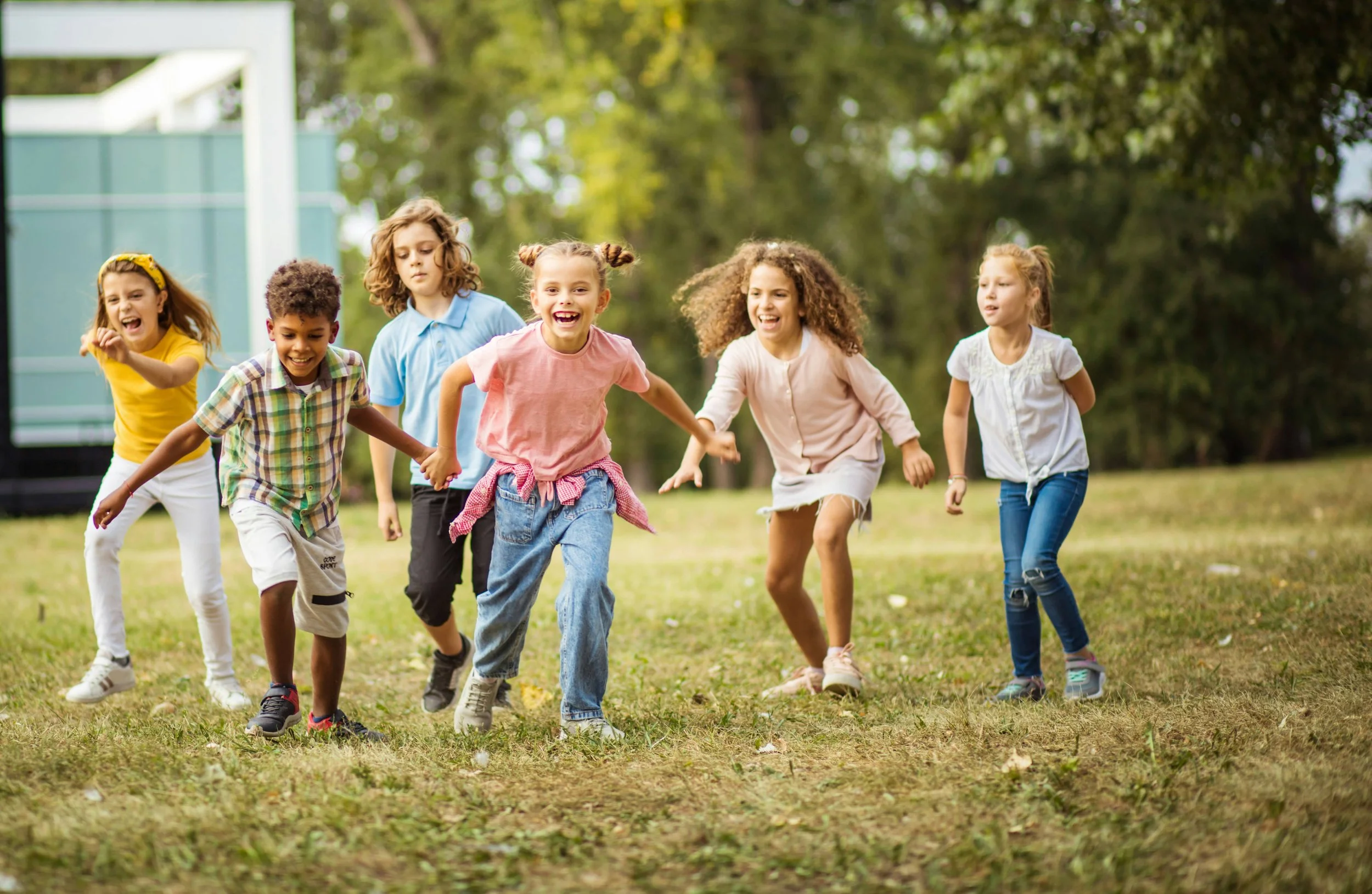 Children running and playing outdoors on a grassy field, holding hands, and smiling.