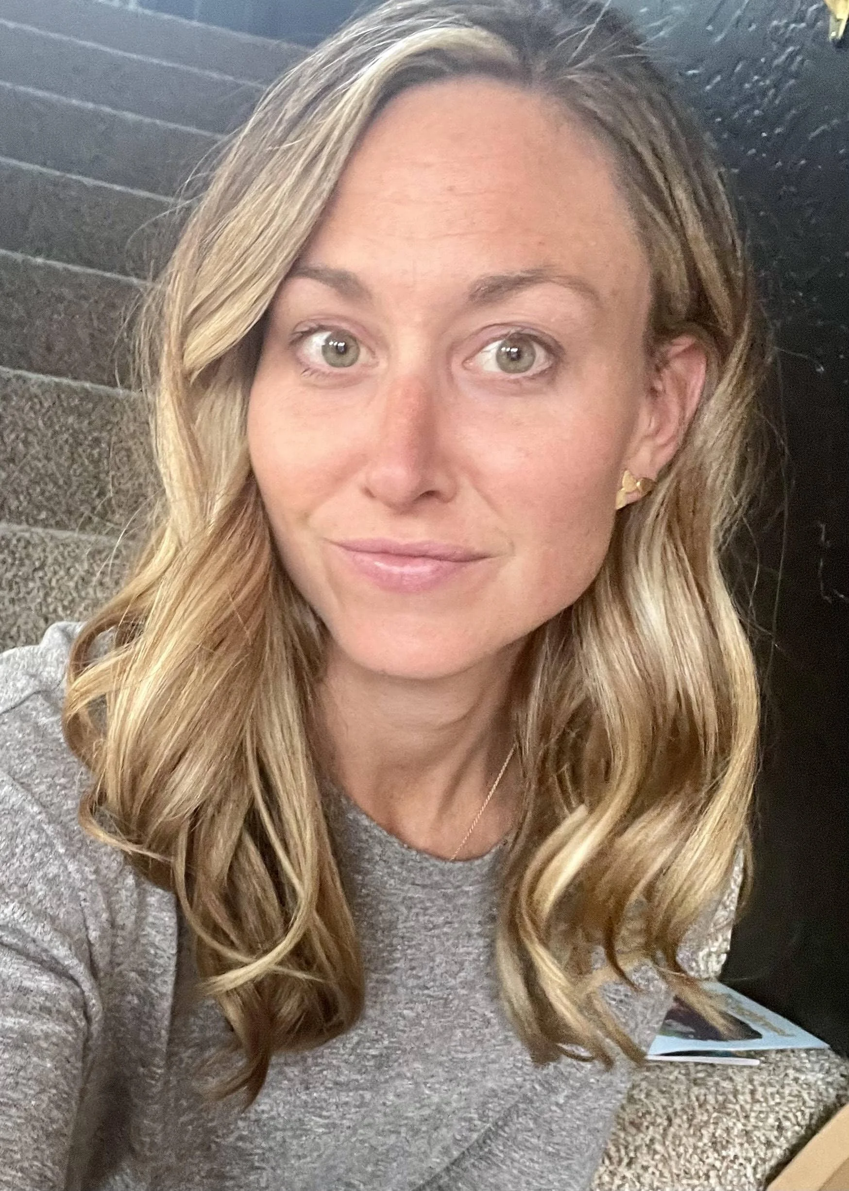 A person with long, wavy blonde hair and light-colored eyes looks into the camera.