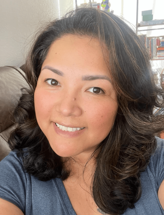 A person with long dark hair and brown eyes is smiling at the camera.