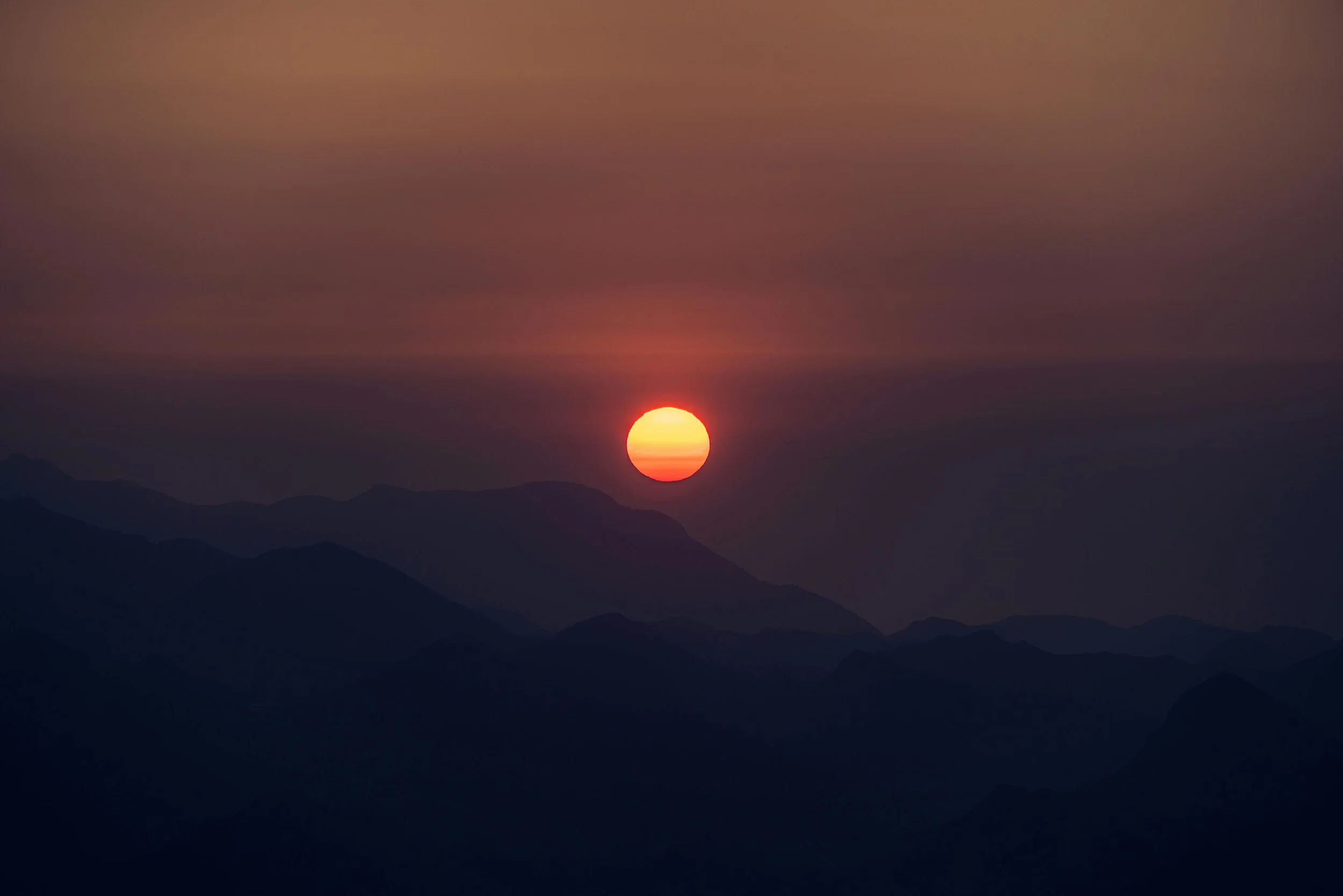 The image shows a sunset over mountain silhouettes, with the sun near the horizon and a warm orange sky.